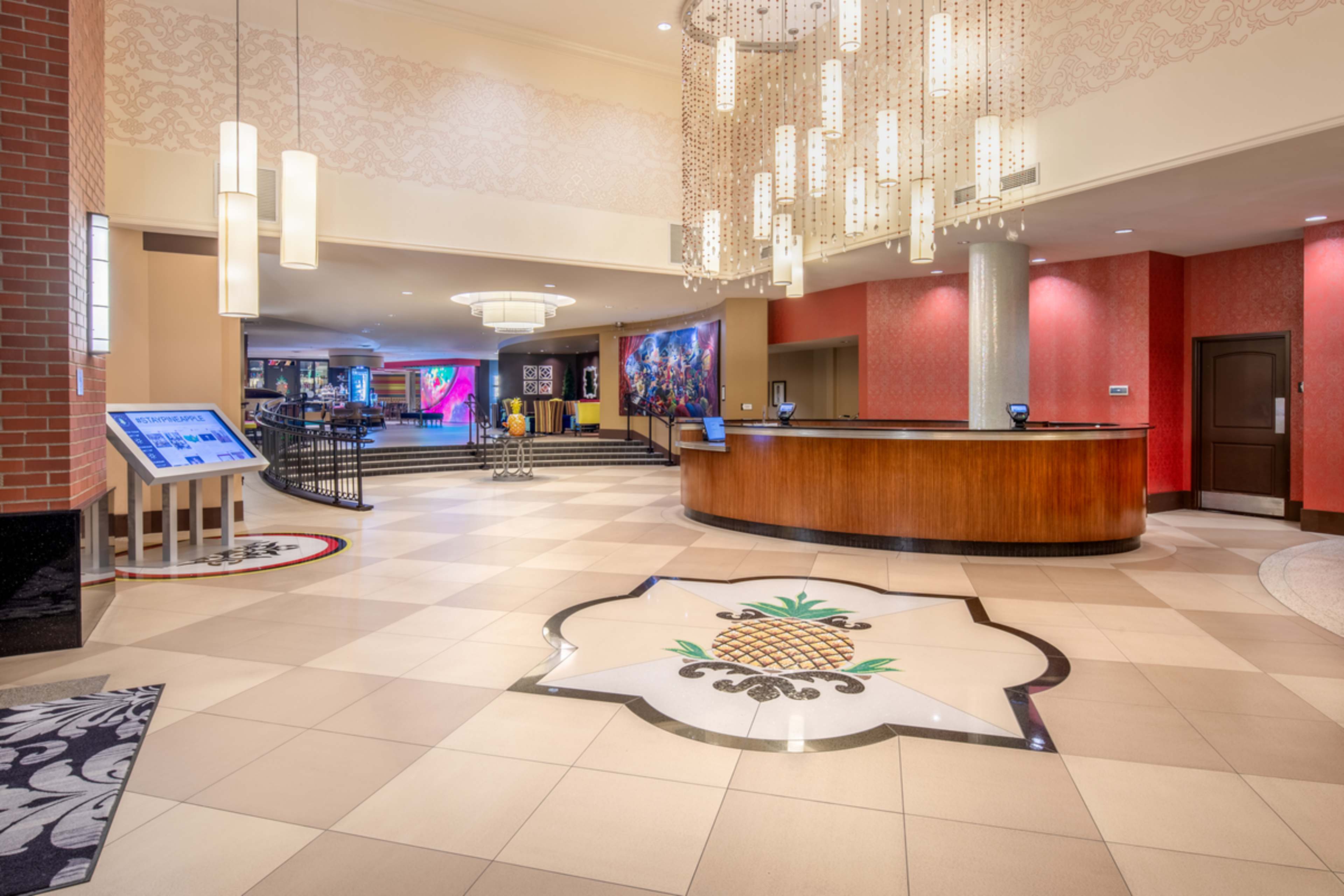 The lobby features a reception desk with a pineapple design inlaid in the tiled floor, surrounded by modern lighting and decorative wall art.
