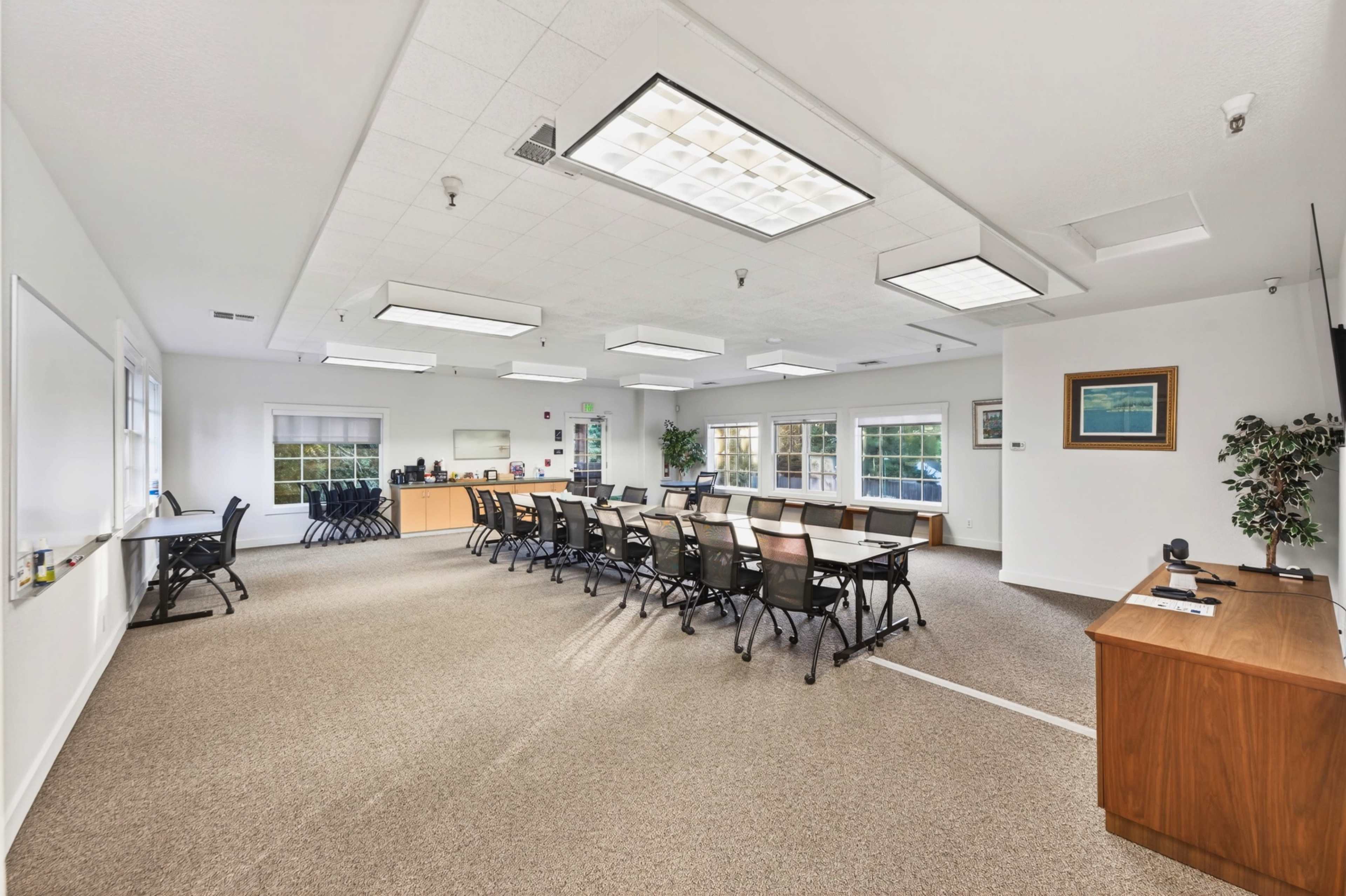 The image shows a well-lit meeting room with a rectangular table set up for discussions, surrounded by chairs, and equipped with a whiteboard and presentation tools.