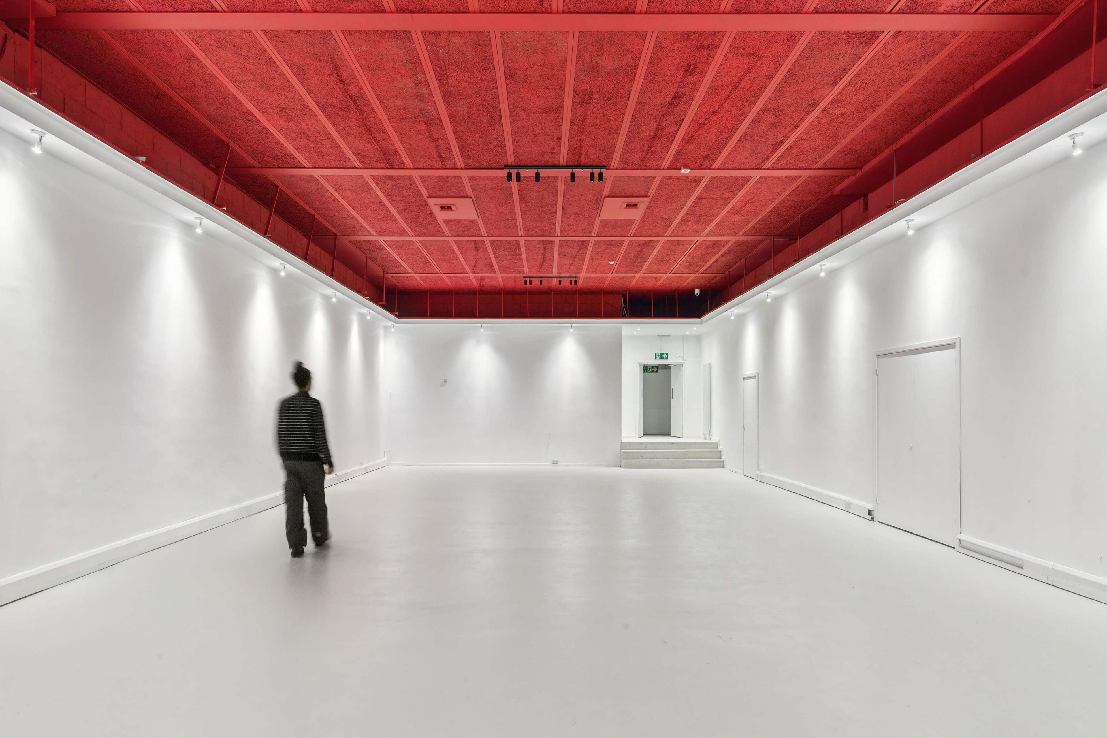 A figure walks through a spacious, minimally decorated white room with a striking red ceiling.