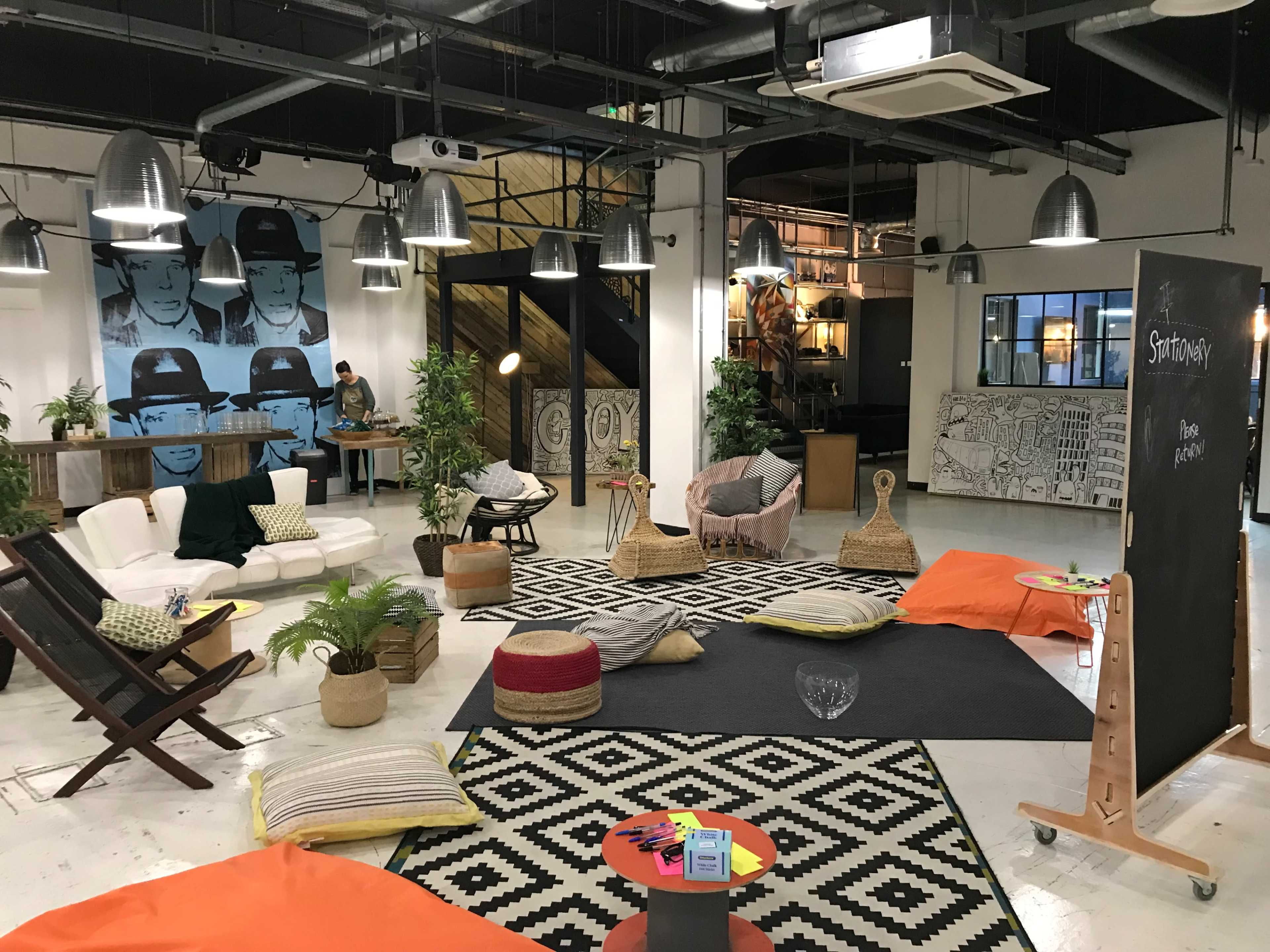A spacious, modern co-working area with various seating options, plants, artwork on the walls, and distinct zones for collaboration and relaxation.