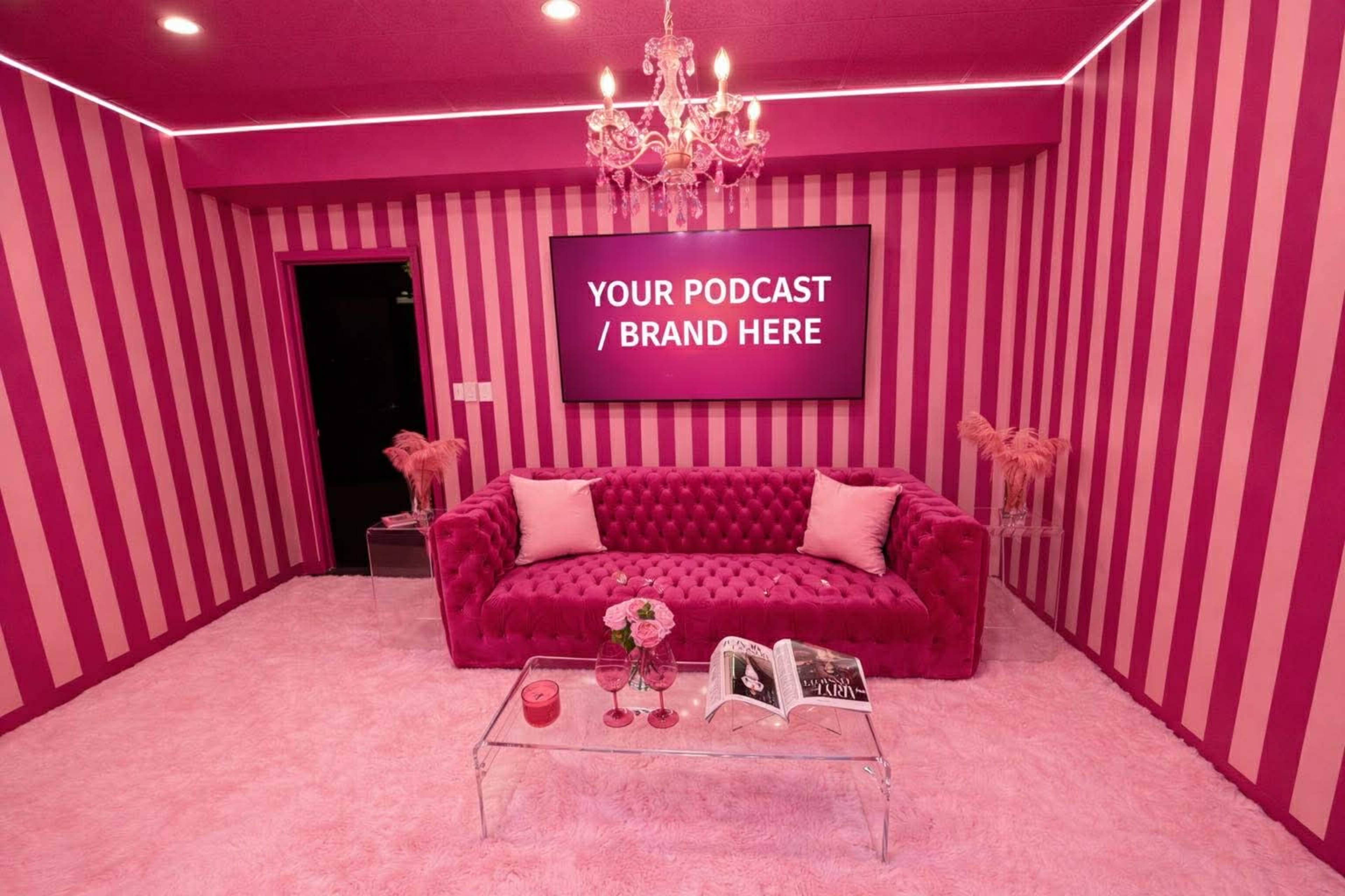 The image depicts a vibrant pink room with striped walls, a plush sofa, a chandelier, and a large screen displaying customizable text, creating a stylish podcasting or branding space.