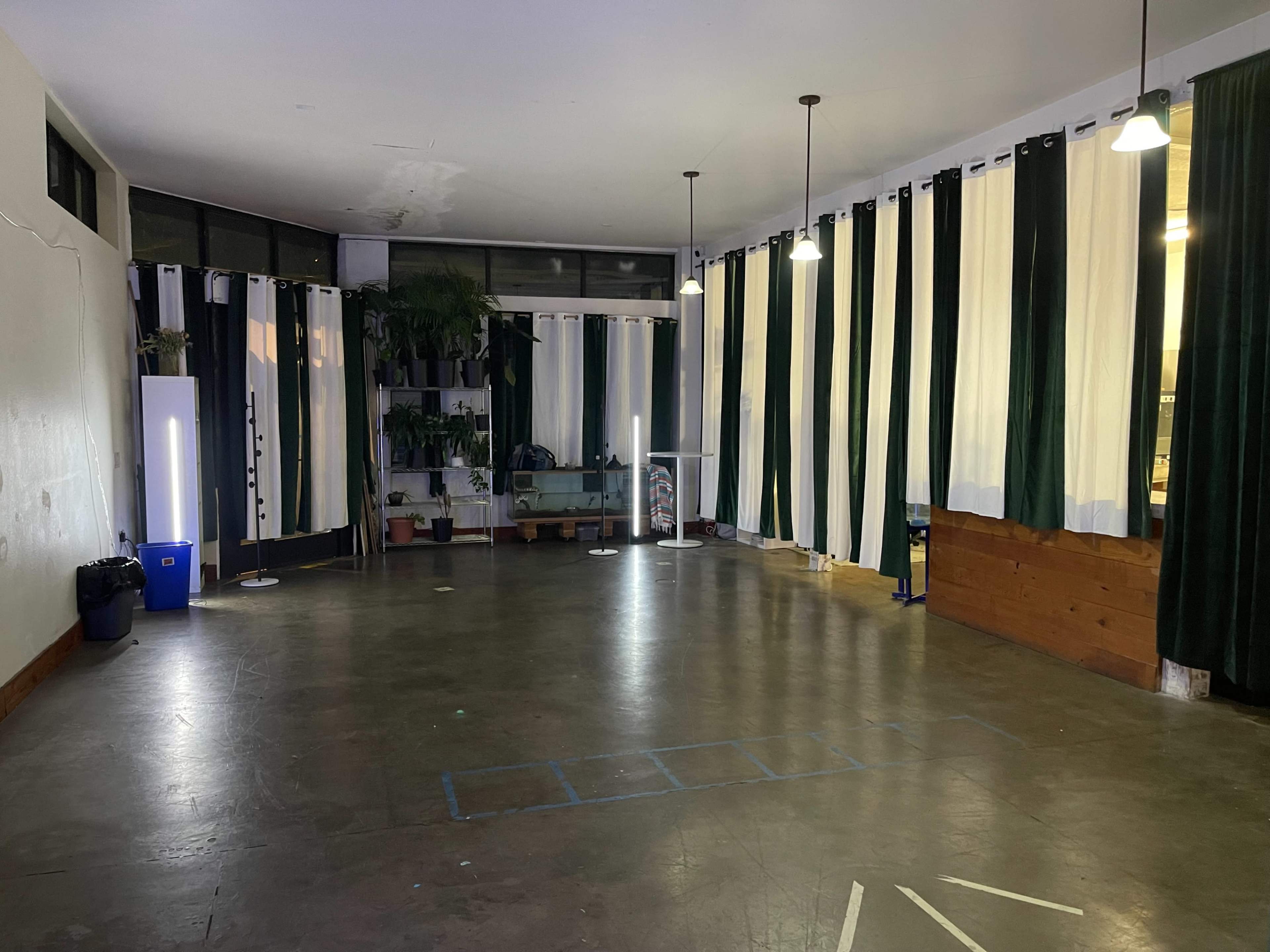 A spacious room with large windows, minimal furnishings, and tall curtains in green and white.