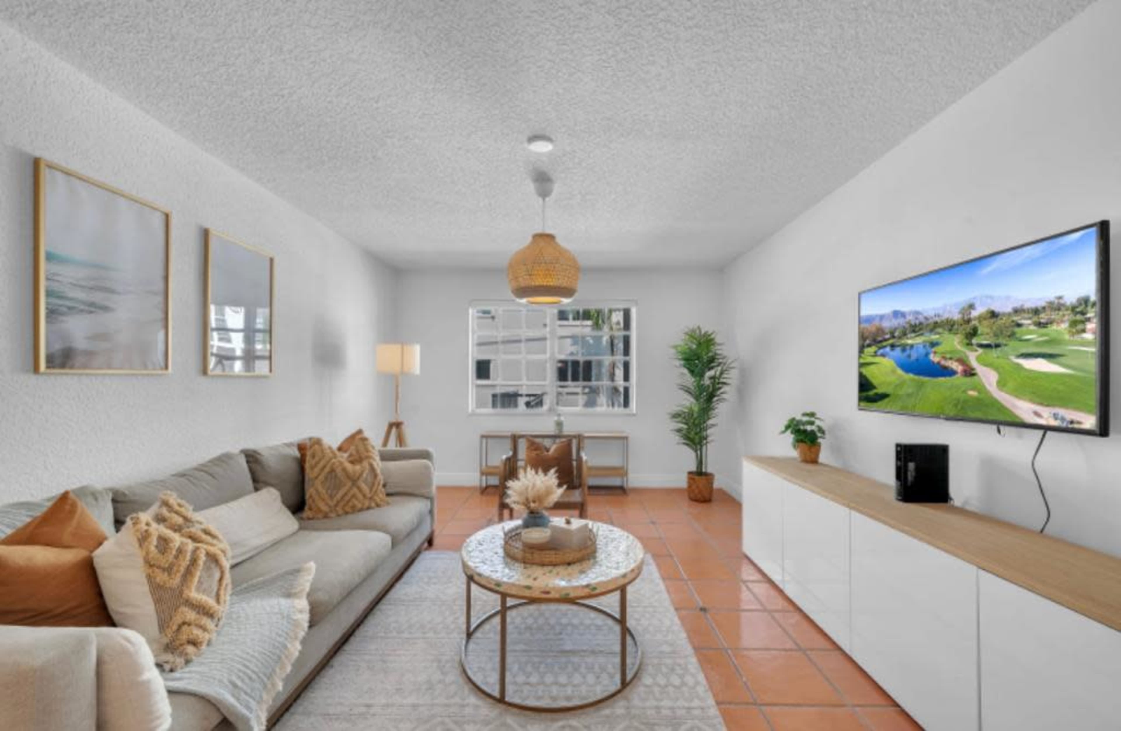 A modern living room with a beige sofa, a round coffee table, a television mounted on the wall, and decorative elements like plants and framed art.