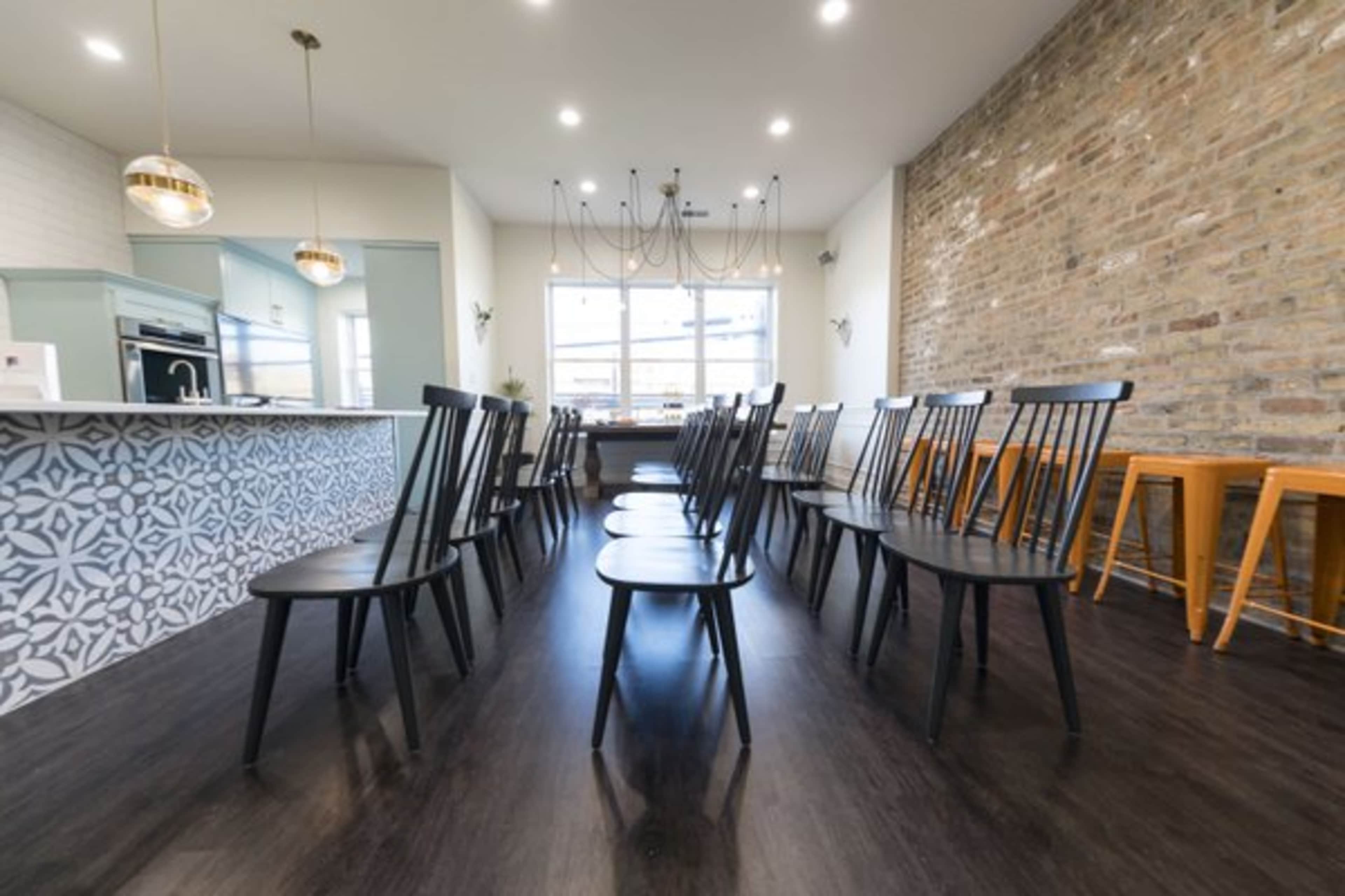 A row of black chairs is set facing a large window in a modern, open space featuring a brick wall and a patterned backsplash.