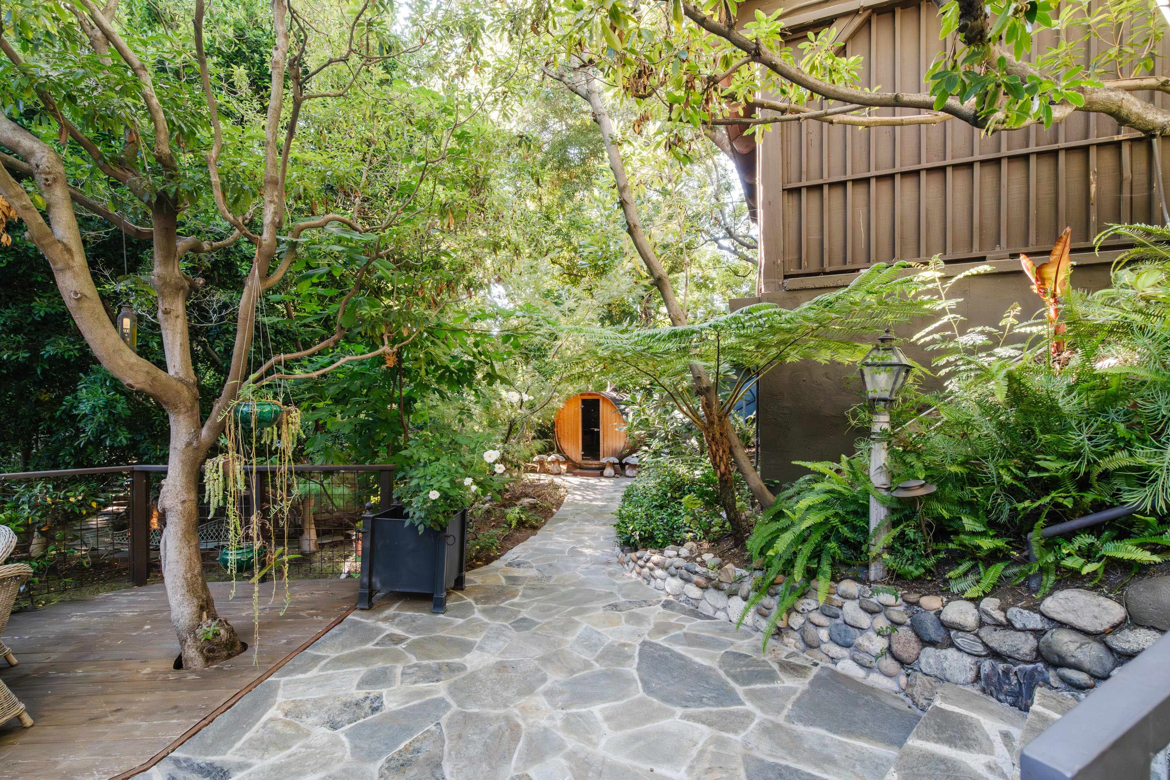 A stone pathway leads through lush greenery to a small wooden structure within a garden setting.