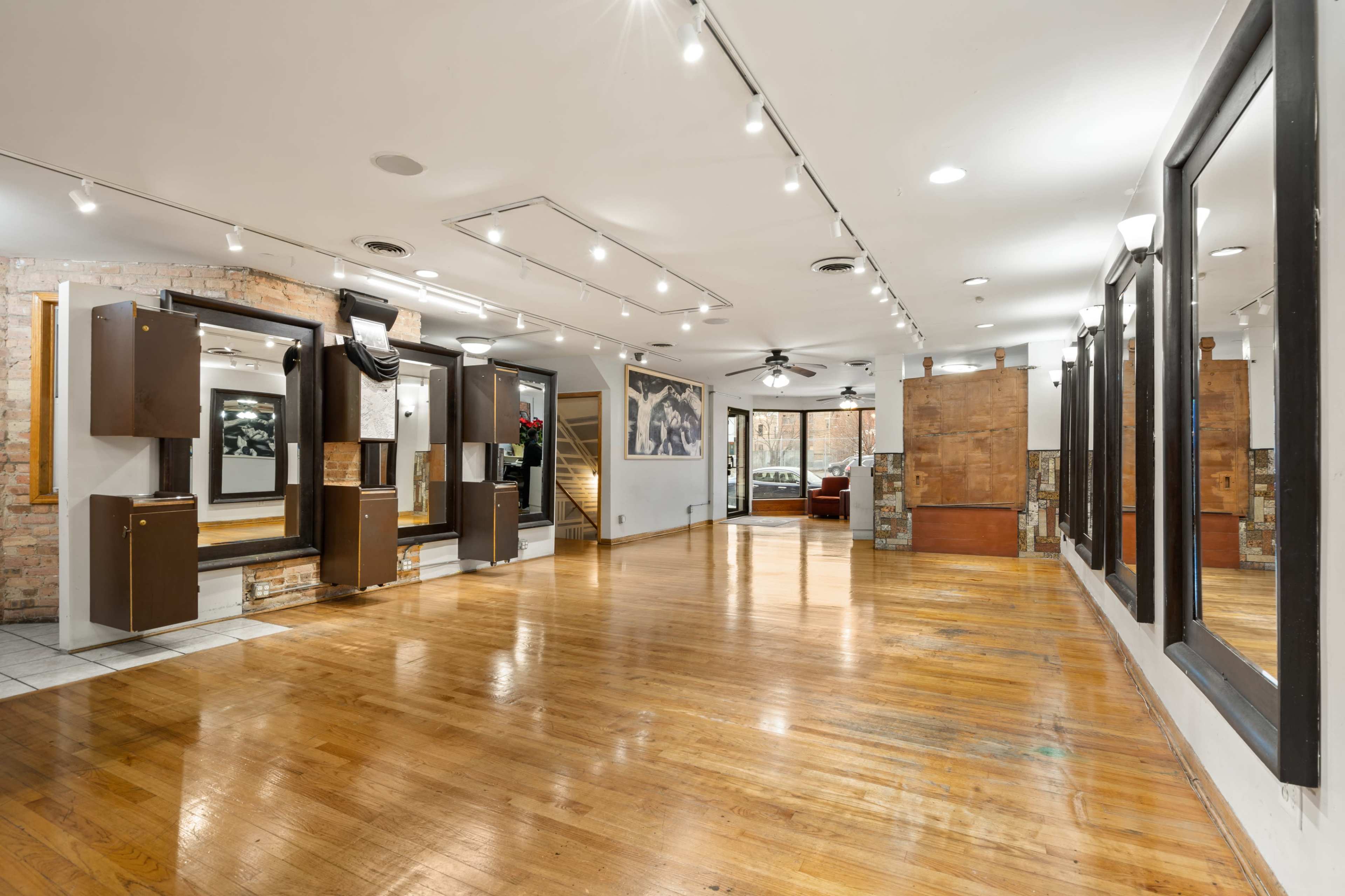 The image shows an empty studio space with wooden floors, large mirrors mounted on the walls, and adjustable lighting.