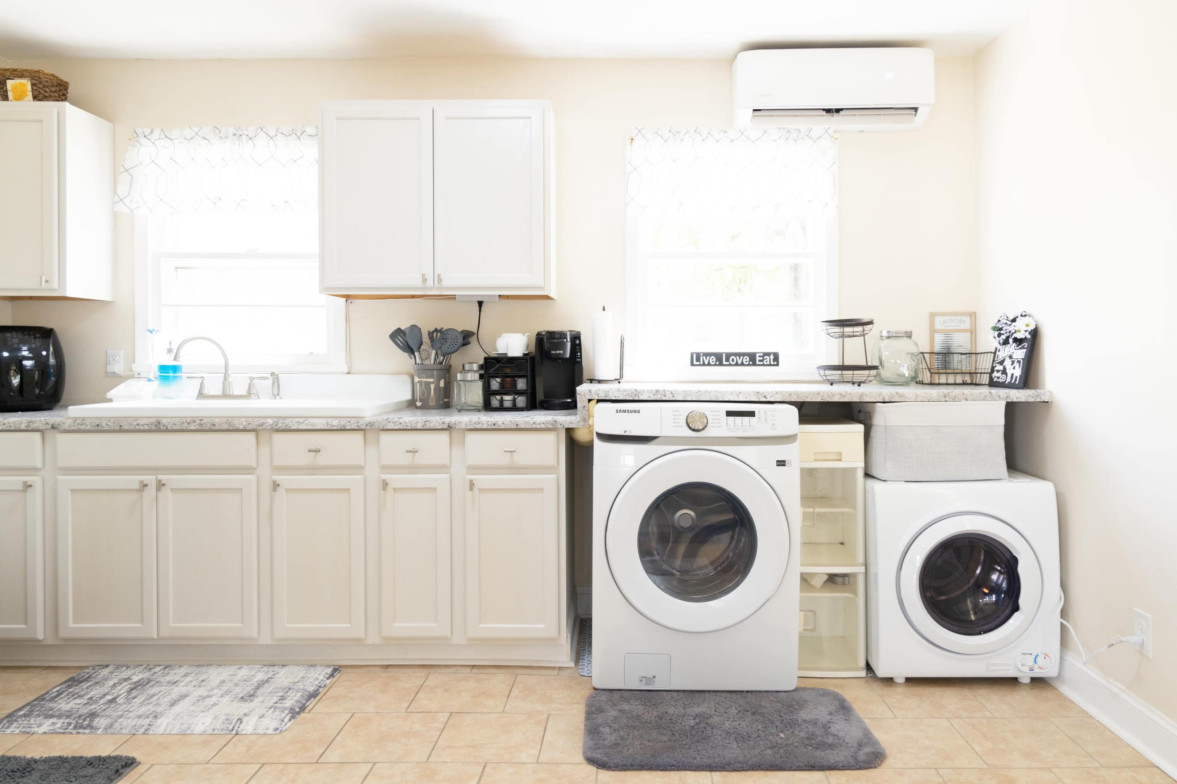 A laundry room with a washing machine, dryer, and a counter next to a sink, featuring cabinets and light-colored walls.