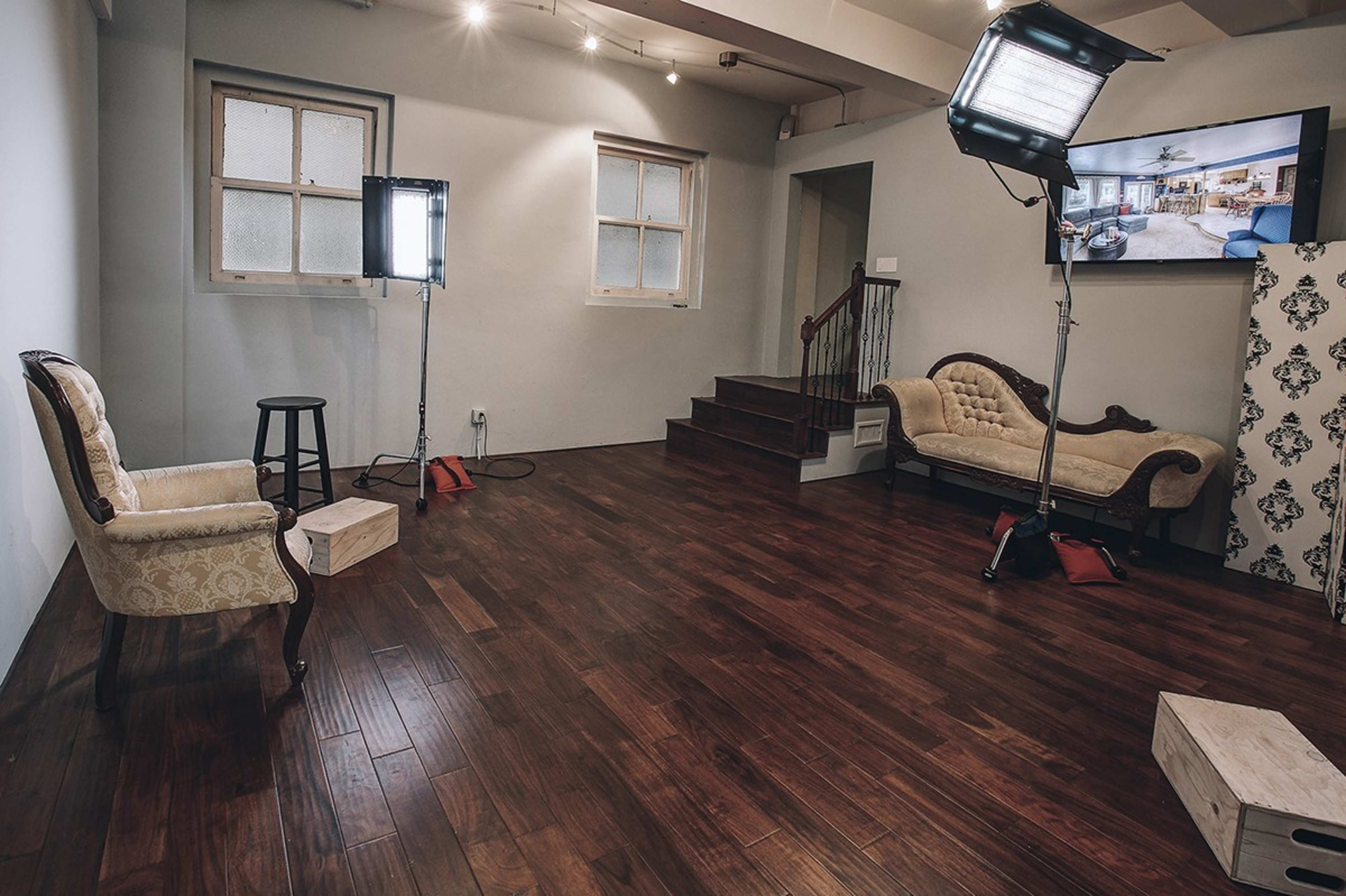 A spacious room with wooden flooring featuring two sofas, a lighting setup, and a staircase in the background.