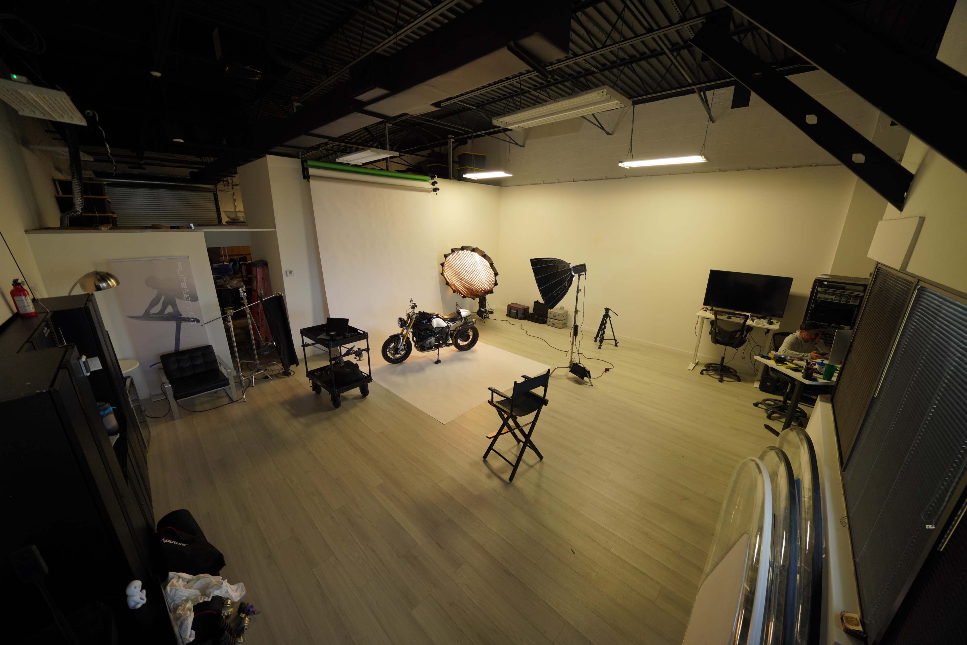 The image shows a photography studio with a motorcycle positioned on a backdrop, surrounded by lighting equipment and various props.