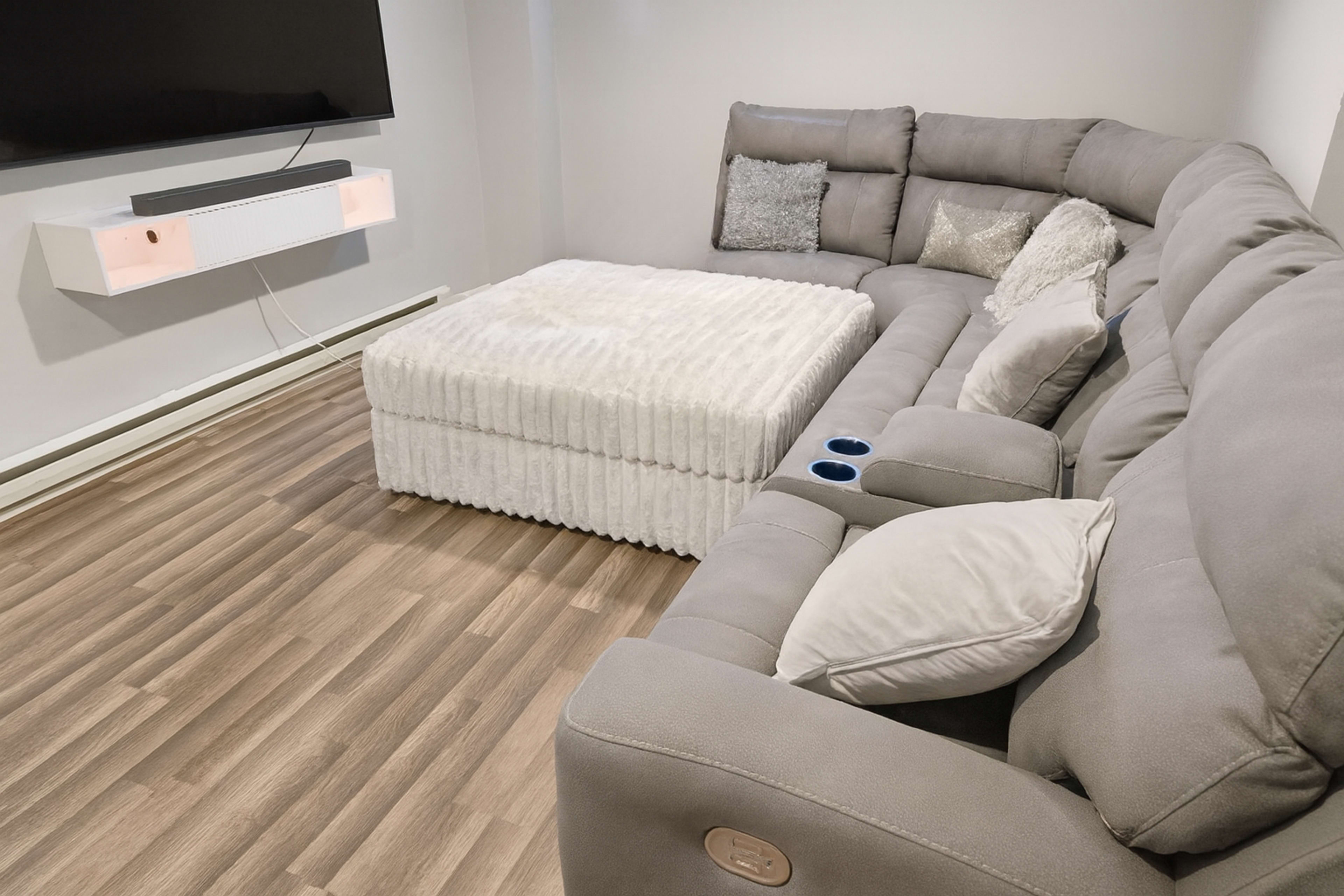 The image shows a sectional sofa in a living room with a coffee table, a mounted television, and light-colored wooden flooring.
