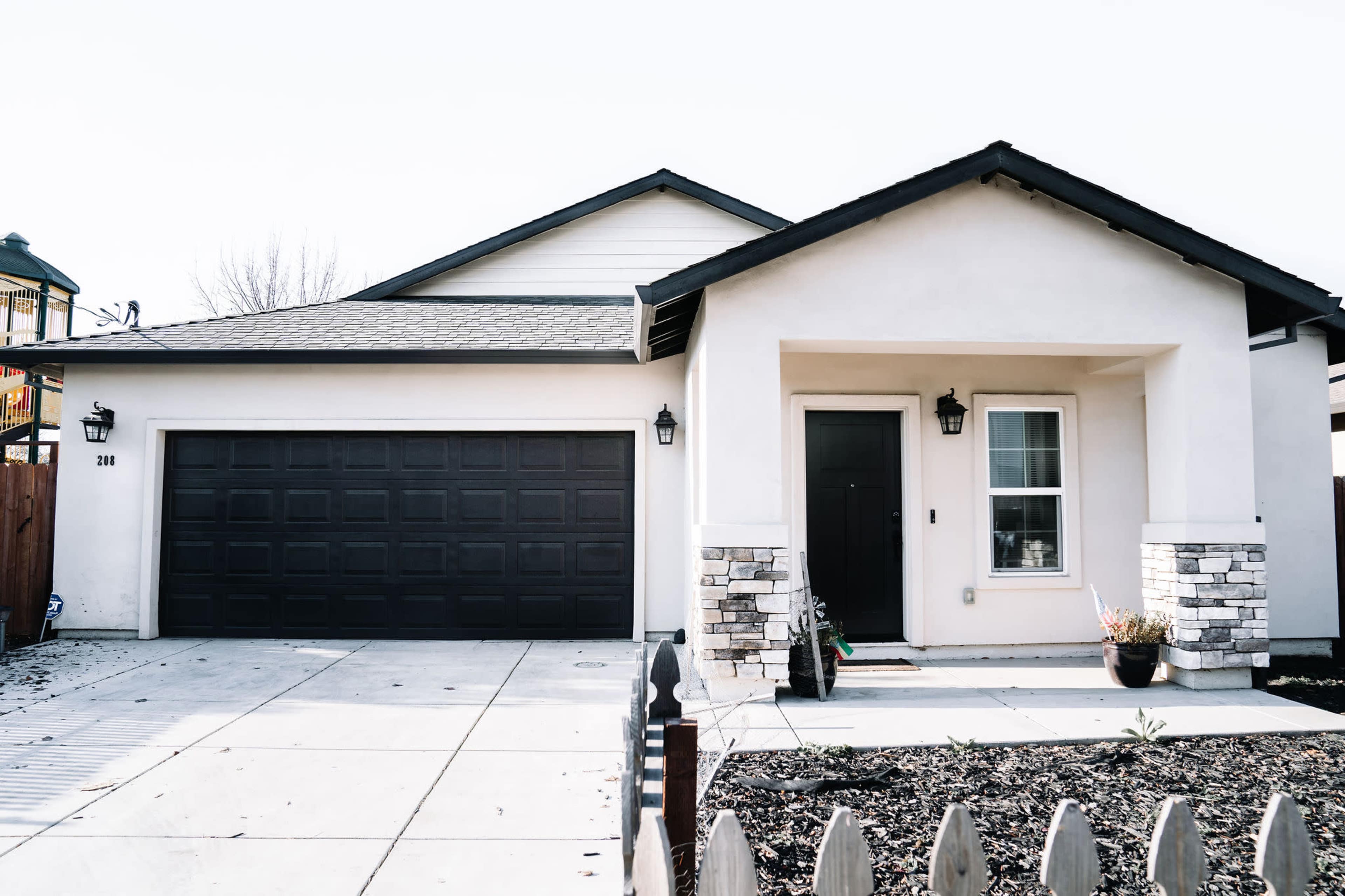 A single-story house with a dark garage door, a light-colored exterior, and stone accents at the entrance.