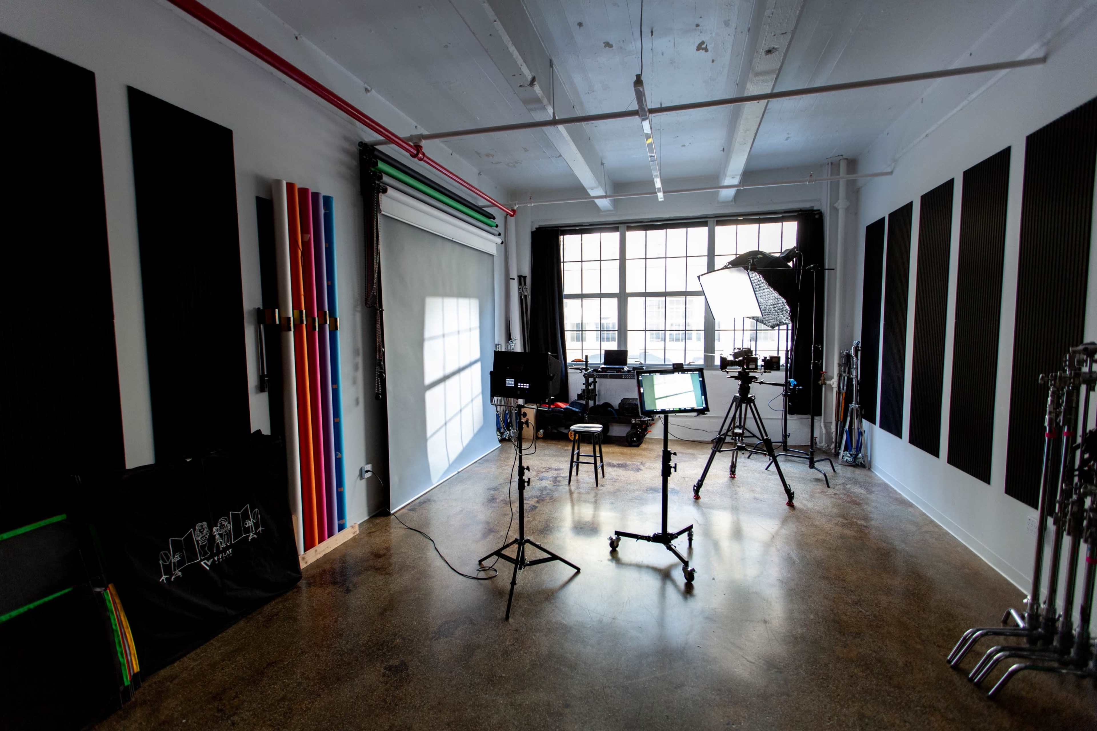 The image shows a photography studio equipped with lighting, backdrops, and cameras set up against a large window.