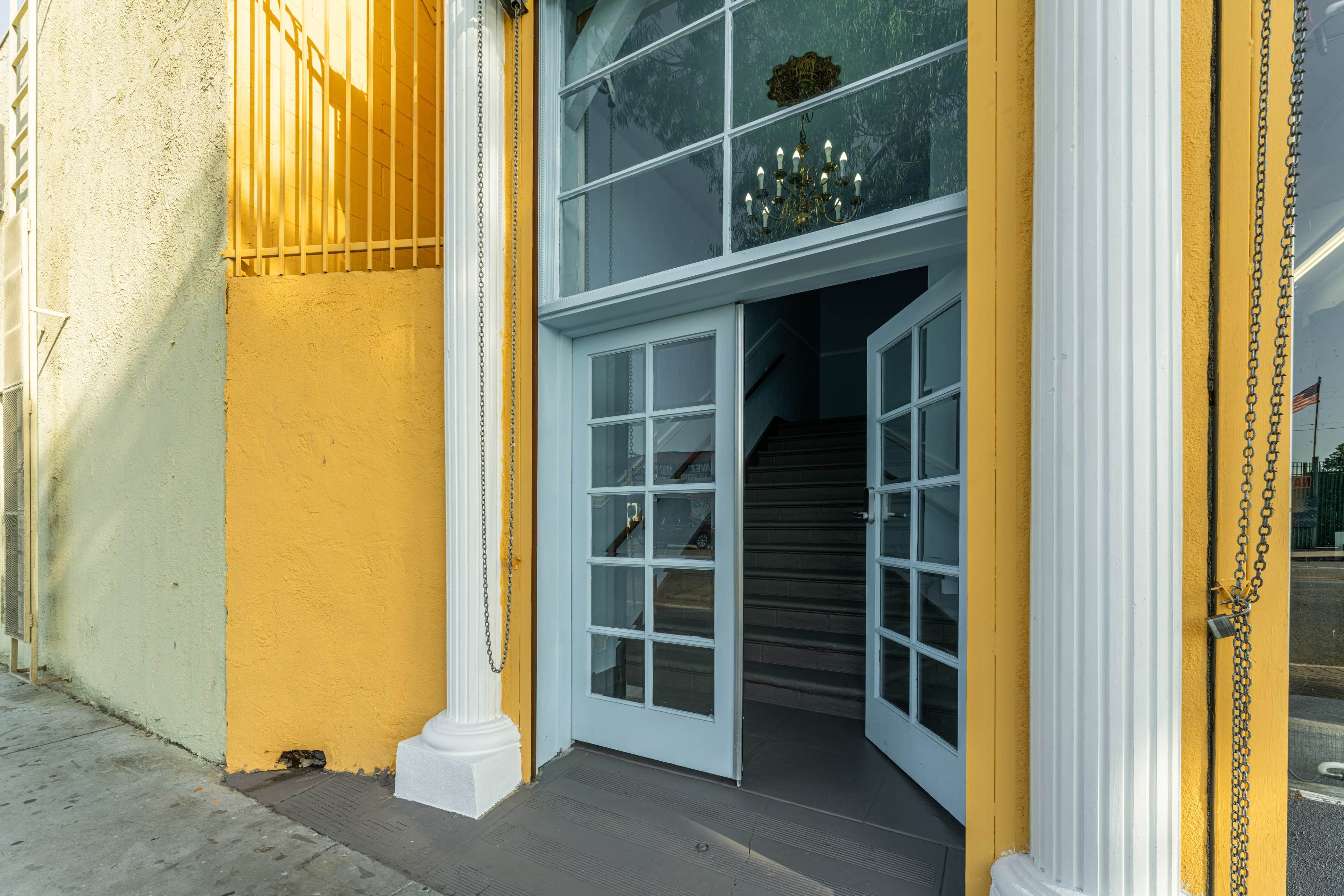 An open double door leading into a building, with a staircase visible inside and yellow-painted columns framing the entrance.