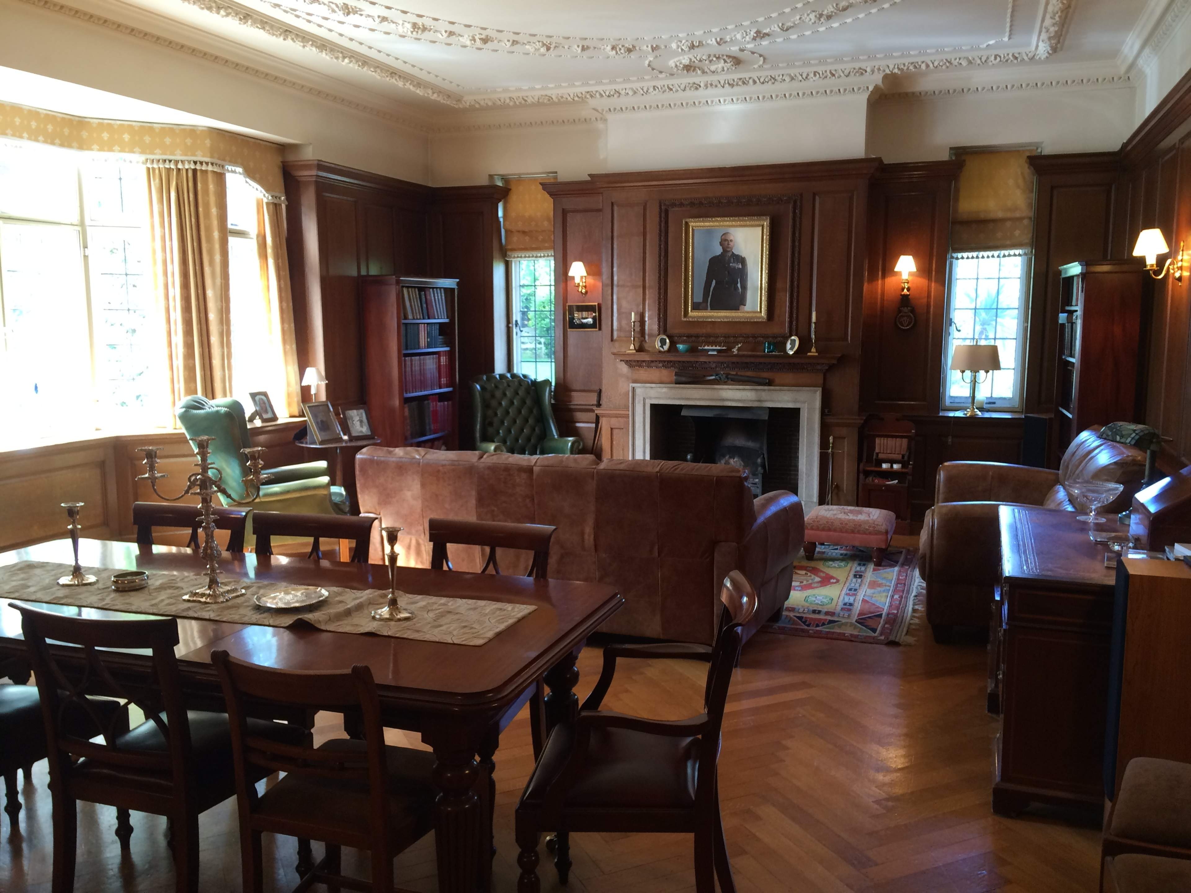 A well-furnished living room with wooden paneling, a fireplace, and various seating arrangements including a green armchair and a brown sofa.