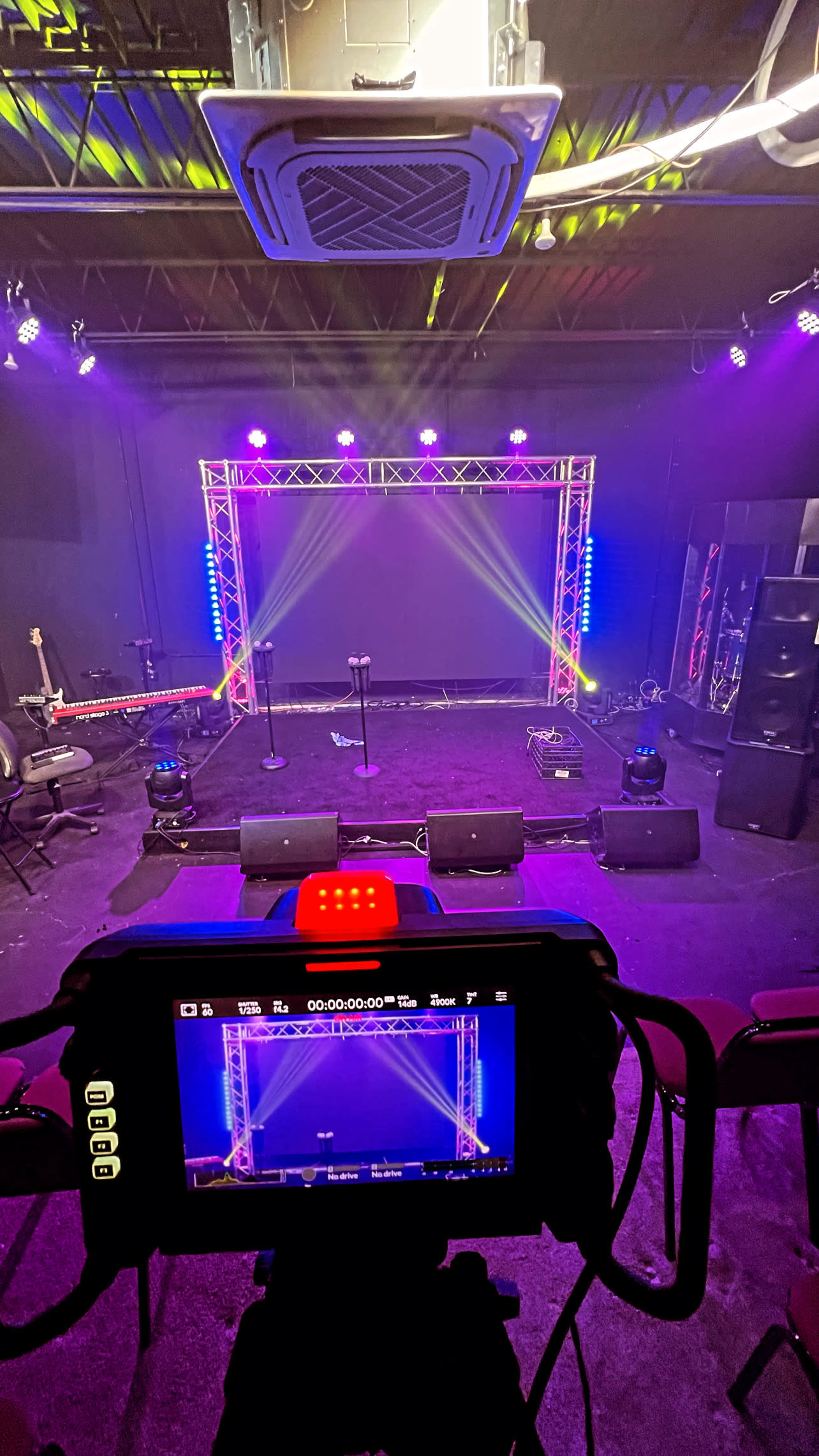 A performance stage setup with lighting and audio equipment, viewed from the perspective of a camera on a tripod.