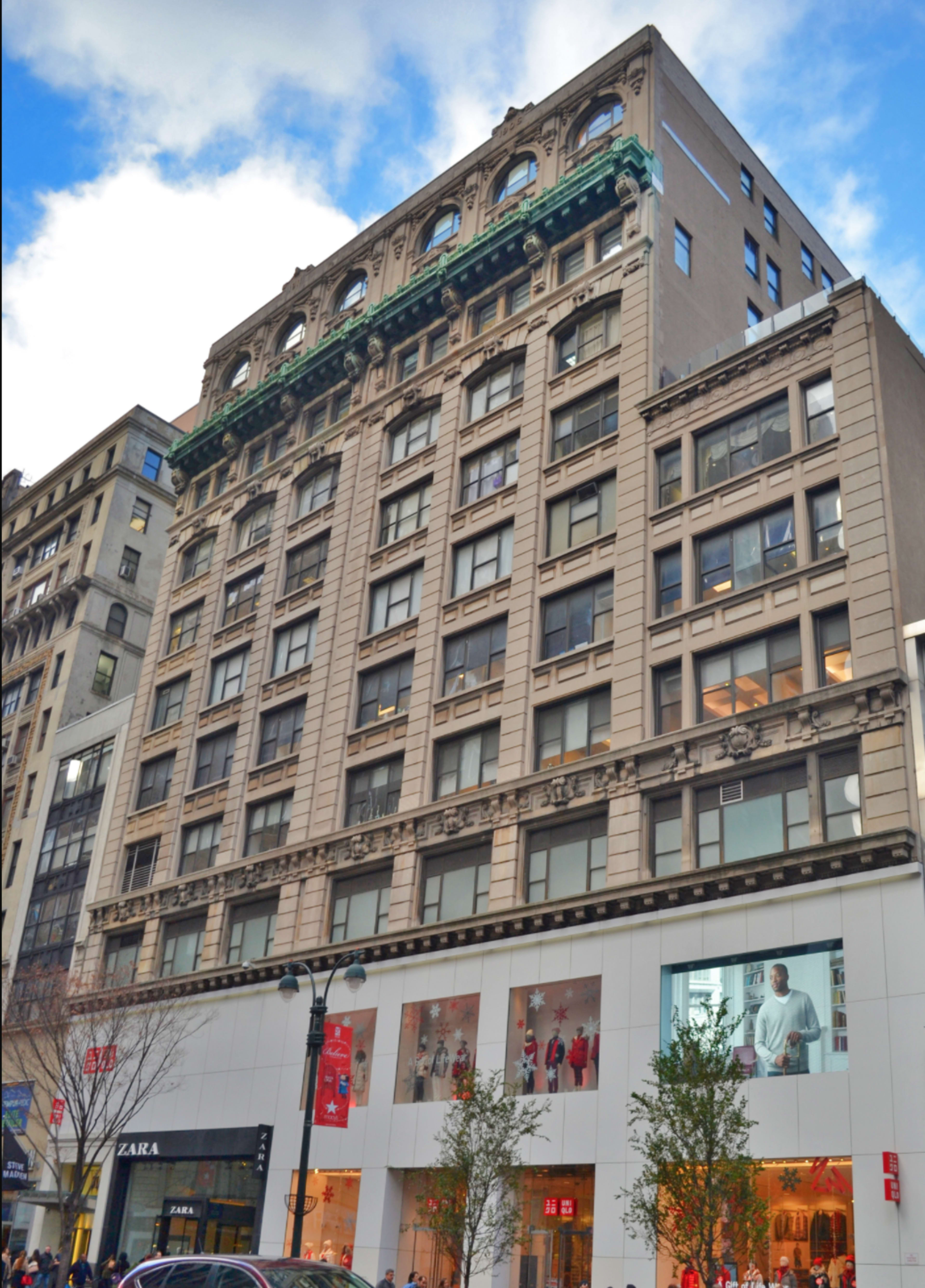 The image shows a historic building with a detailed façade featuring several floors of windows, topped by a decorative cornice, and a retail storefront at ground level.