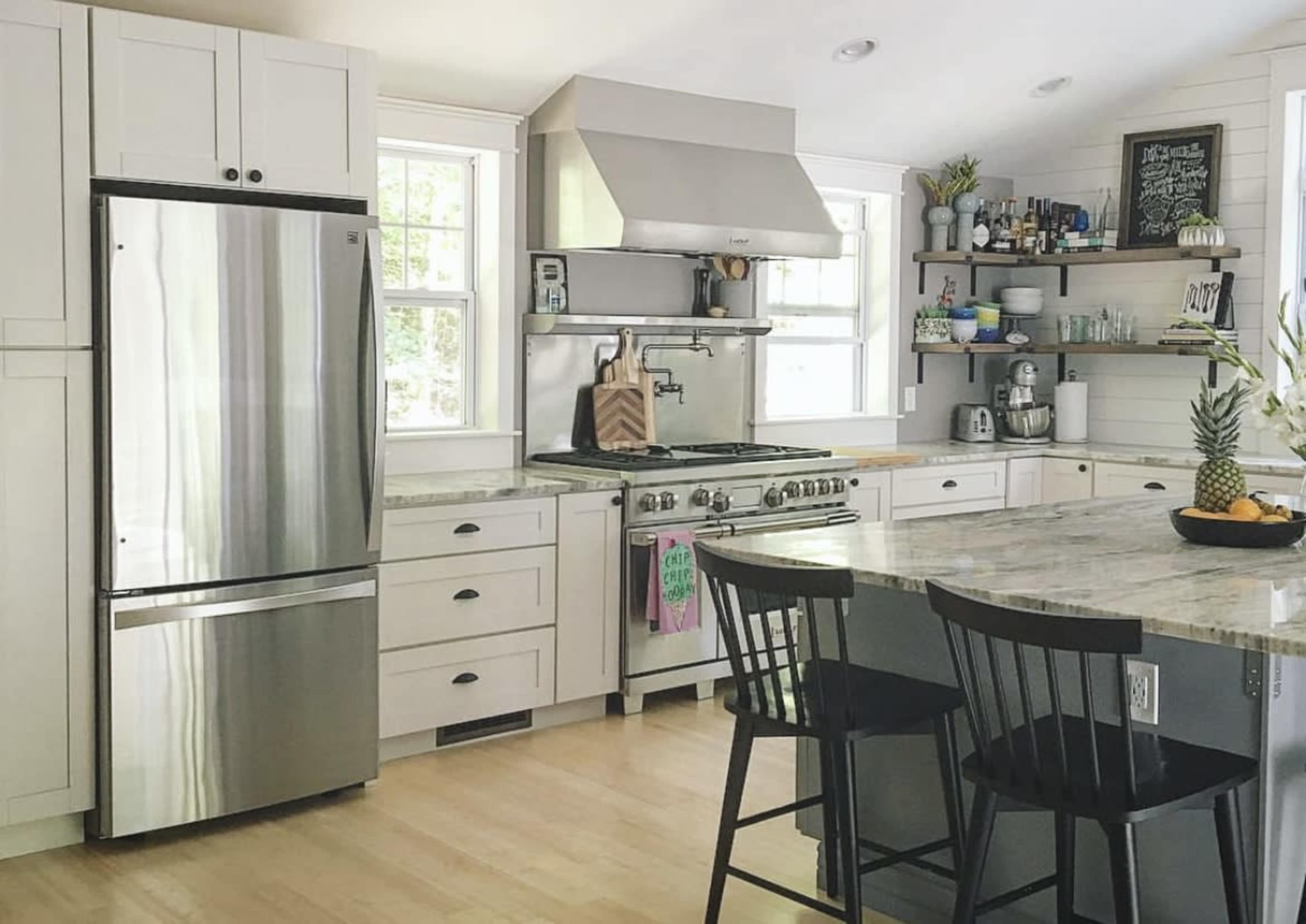 A modern kitchen with stainless steel appliances, a marble countertop, and open shelving displaying various kitchen items.