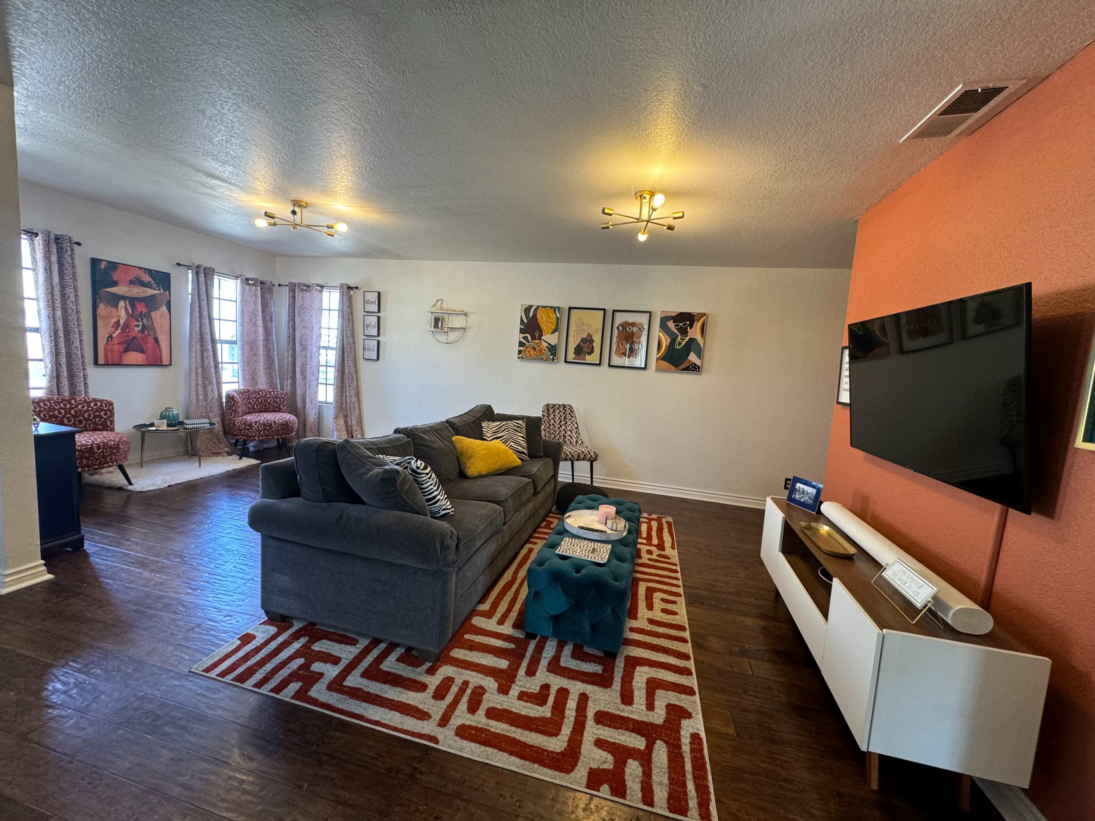 The living room features a gray sectional sofa, a large television mounted on a white media console, and decorative artwork on the walls.