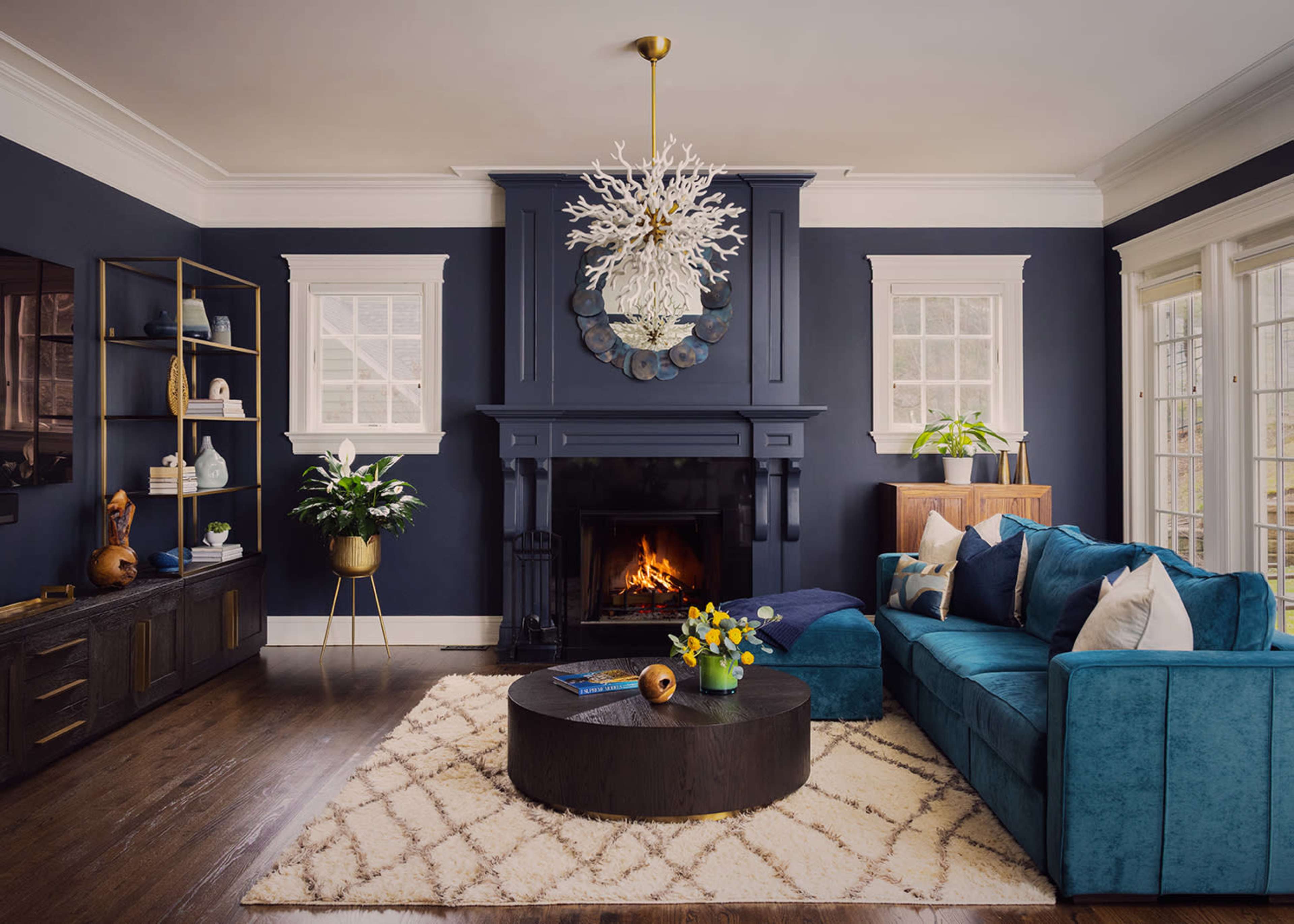The living room features a navy blue accent wall, a fireplace with a decorative mantel, a large turquoise sectional sofa, and a round coffee table on a light-colored rug.