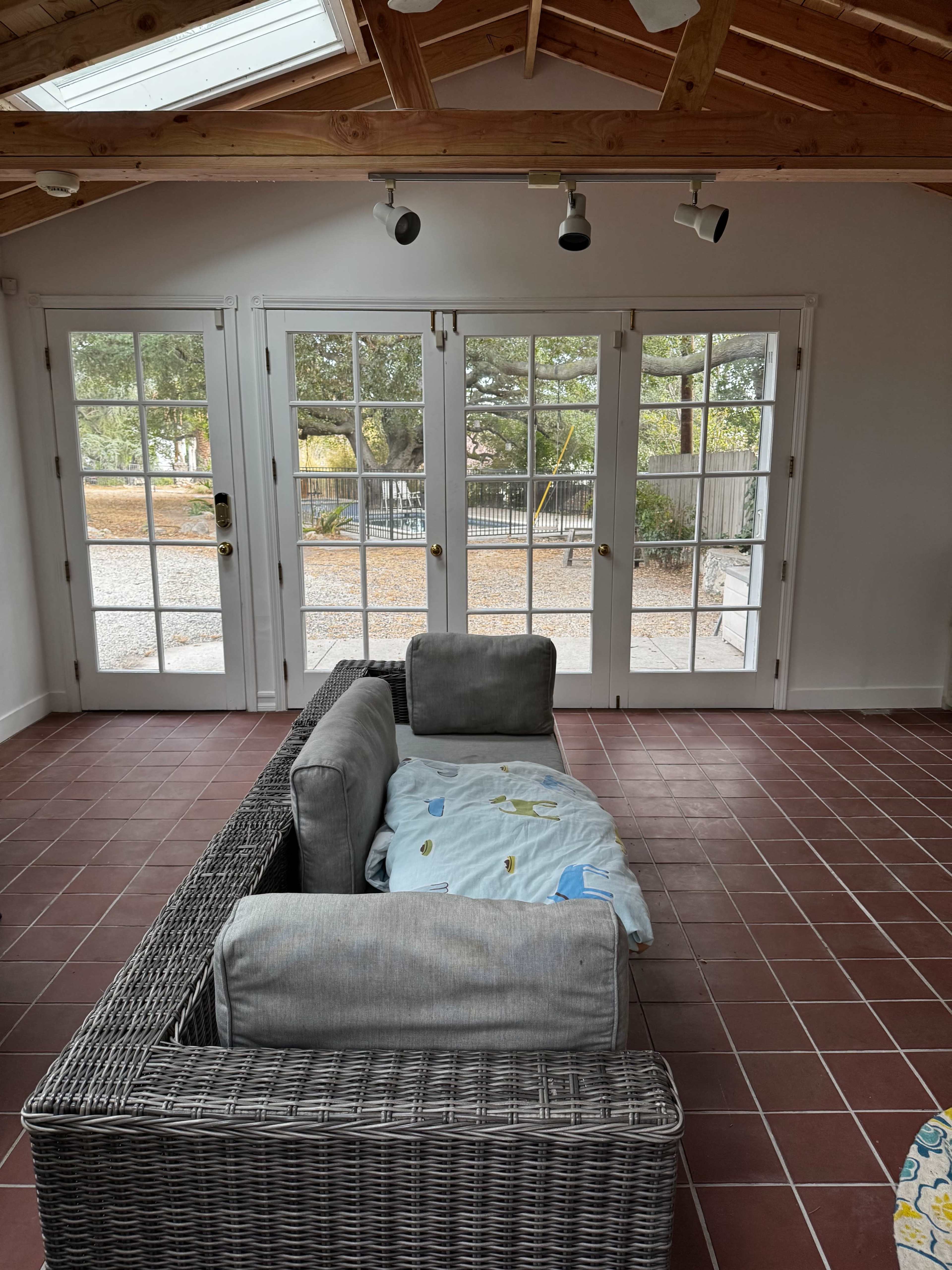The image shows a room with a gray wicker sofa facing multiple glass-paneled doors that open to an outdoor area with gravel.