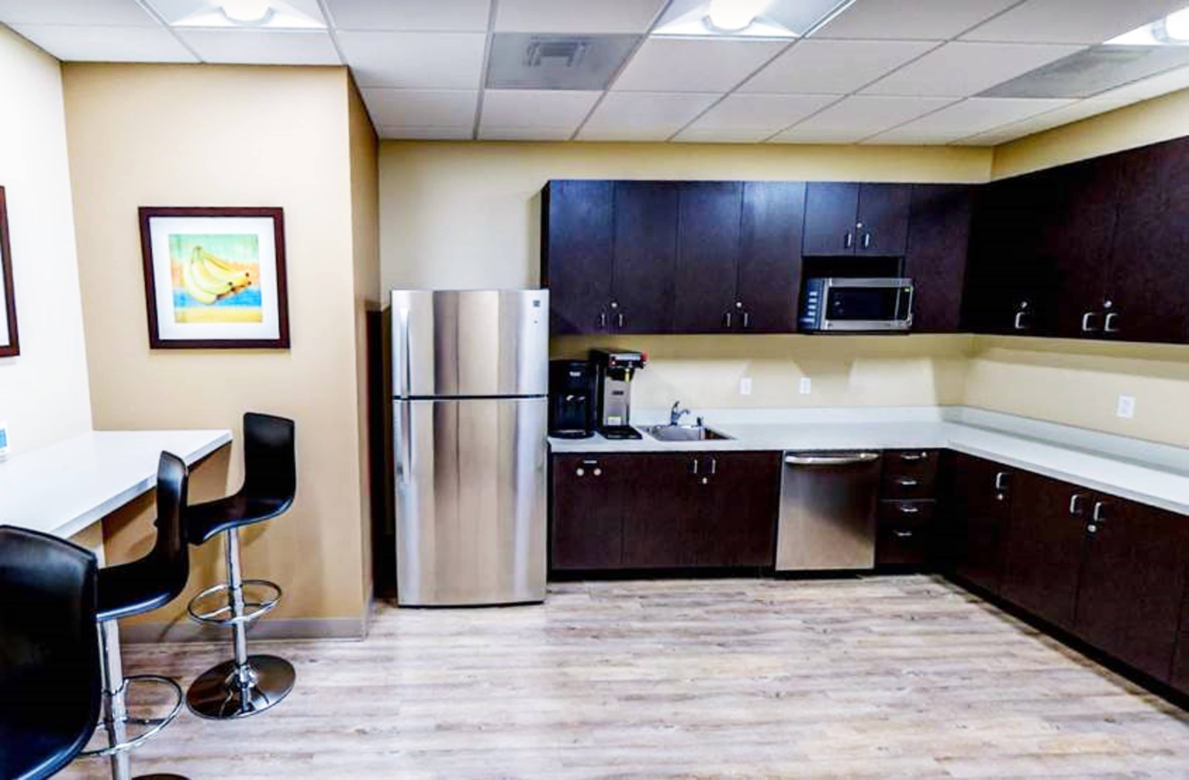 A modern kitchen with stainless steel appliances, dark wood cabinetry, and a small seating area with bar stools.