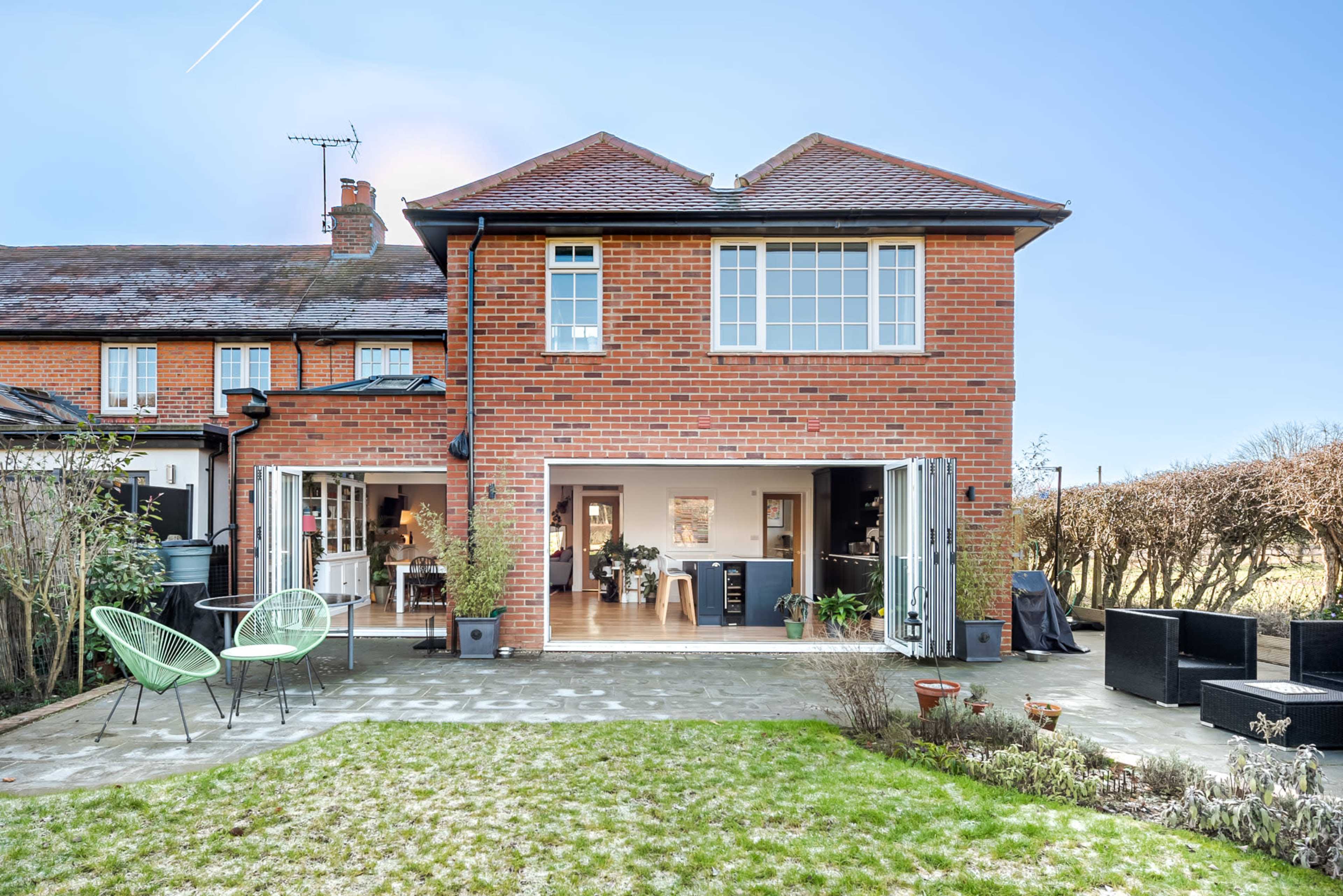 A two-story brick home with large folding doors opens to a patio and a well-kept garden.