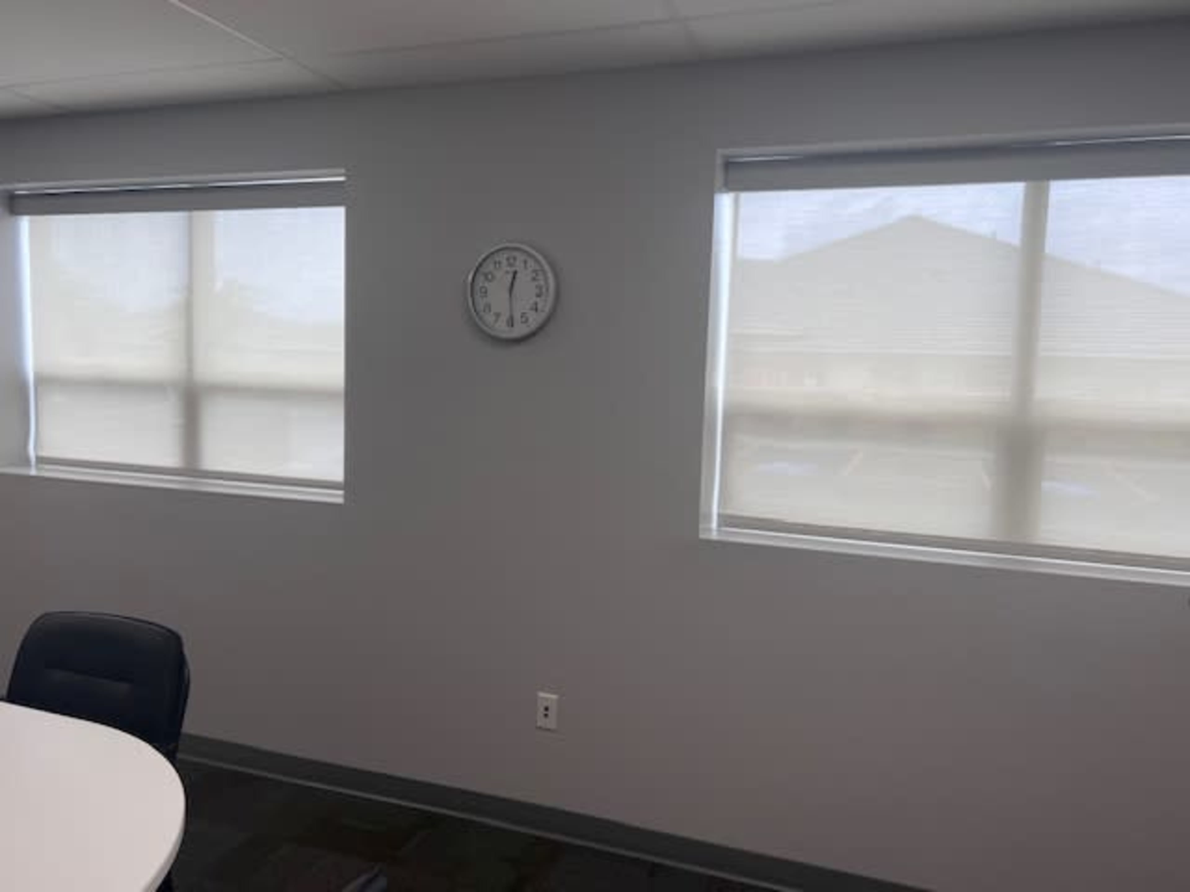 A minimalist office space with two windows, a clock on the wall, and a round table.