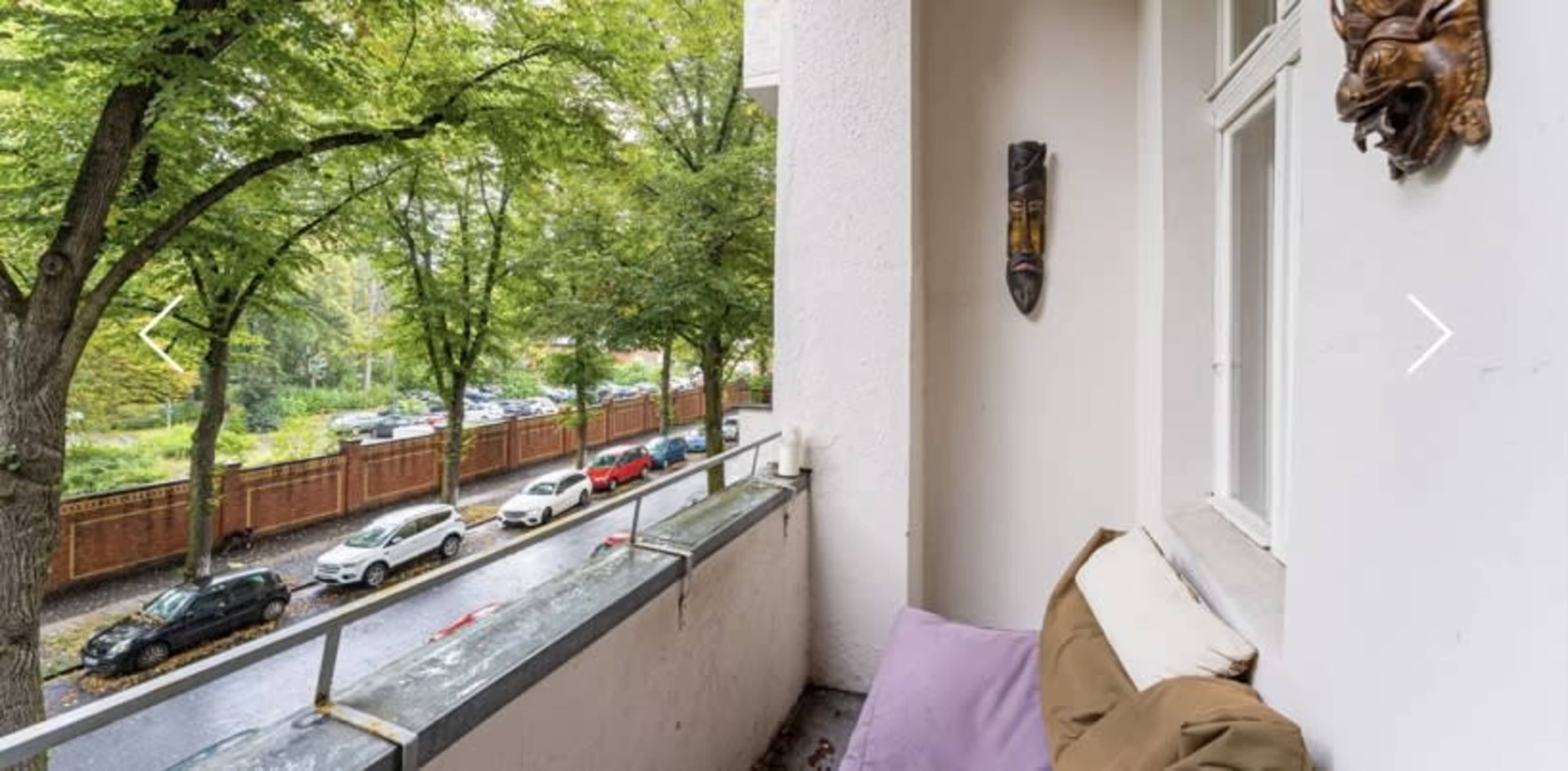 A balcony with a view of trees and parked cars along a street below.