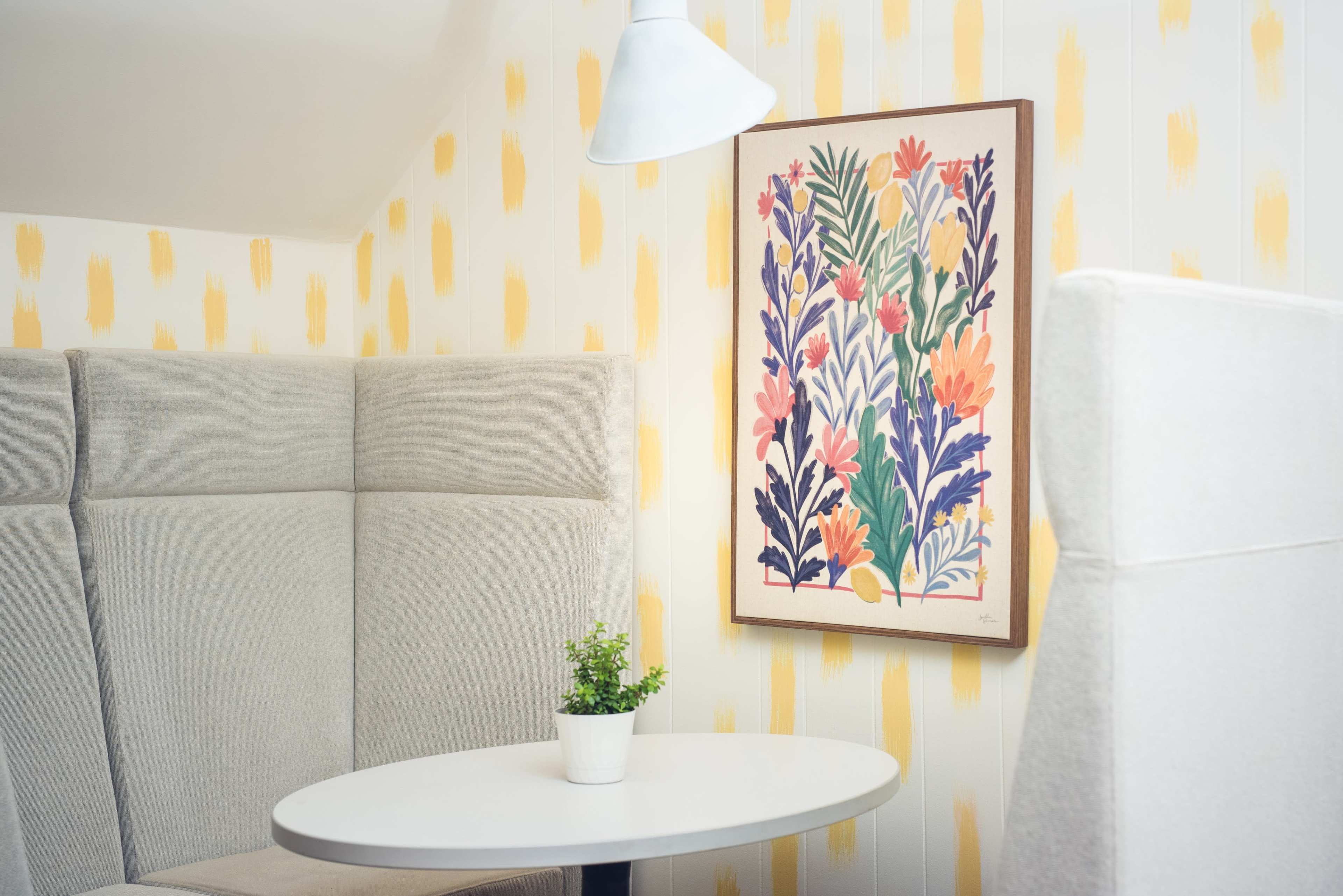 A cozy seating area with gray upholstered walls, a round white table, and a colorful floral artwork hanging above.