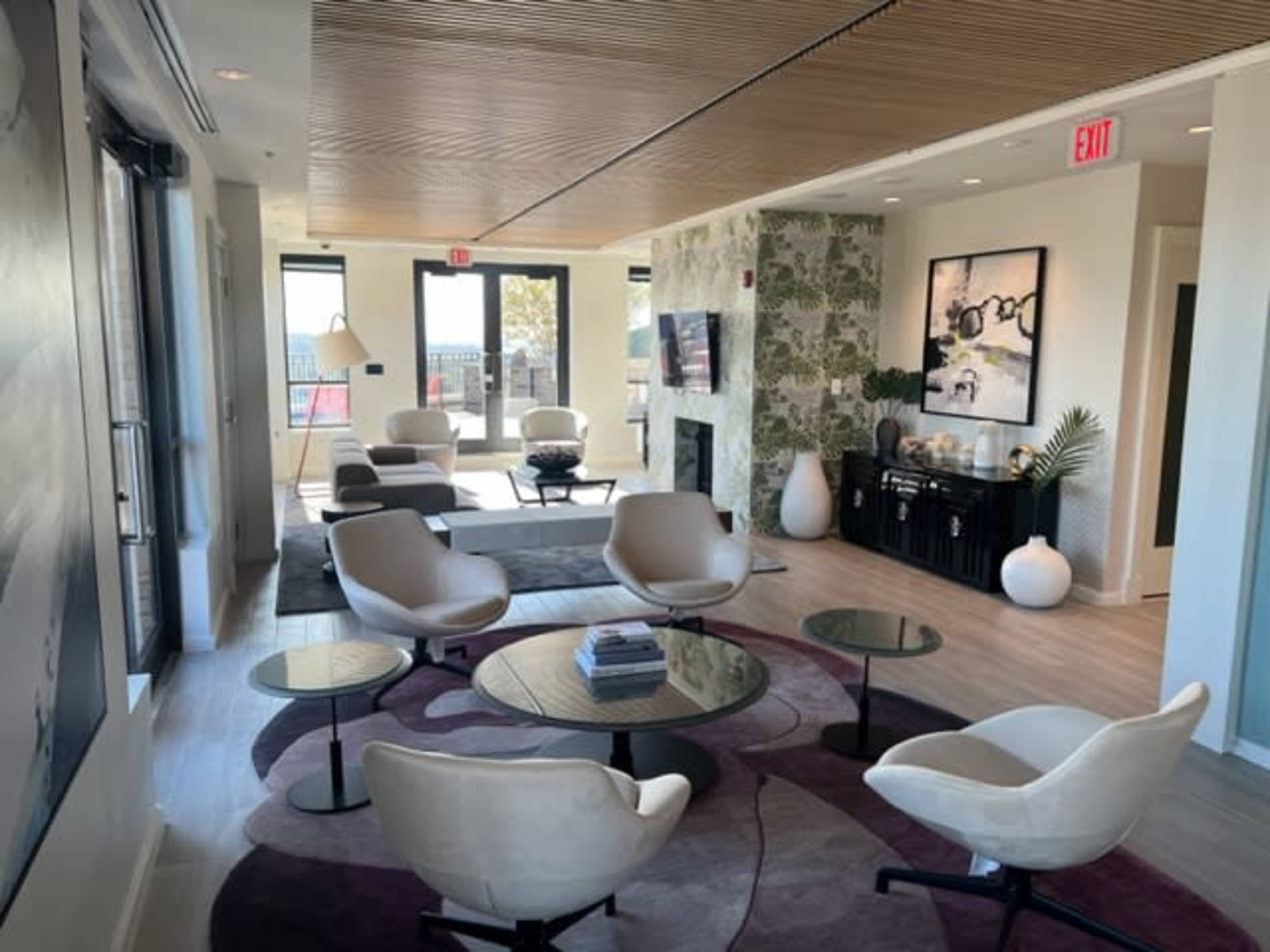 A modern lounge area with several seating options, a fireplace, and large windows allowing natural light to enter.