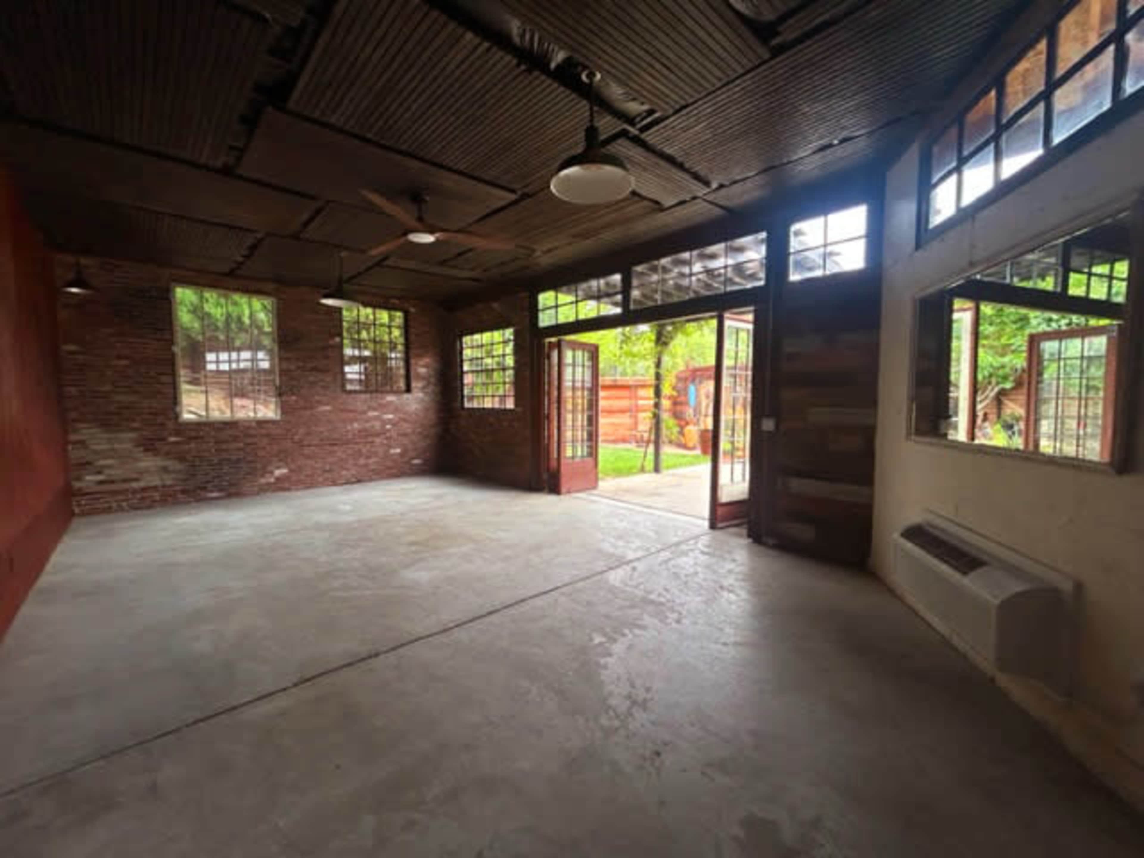 An empty room with exposed brick walls, large windows, and double doors leading to an outdoor area.