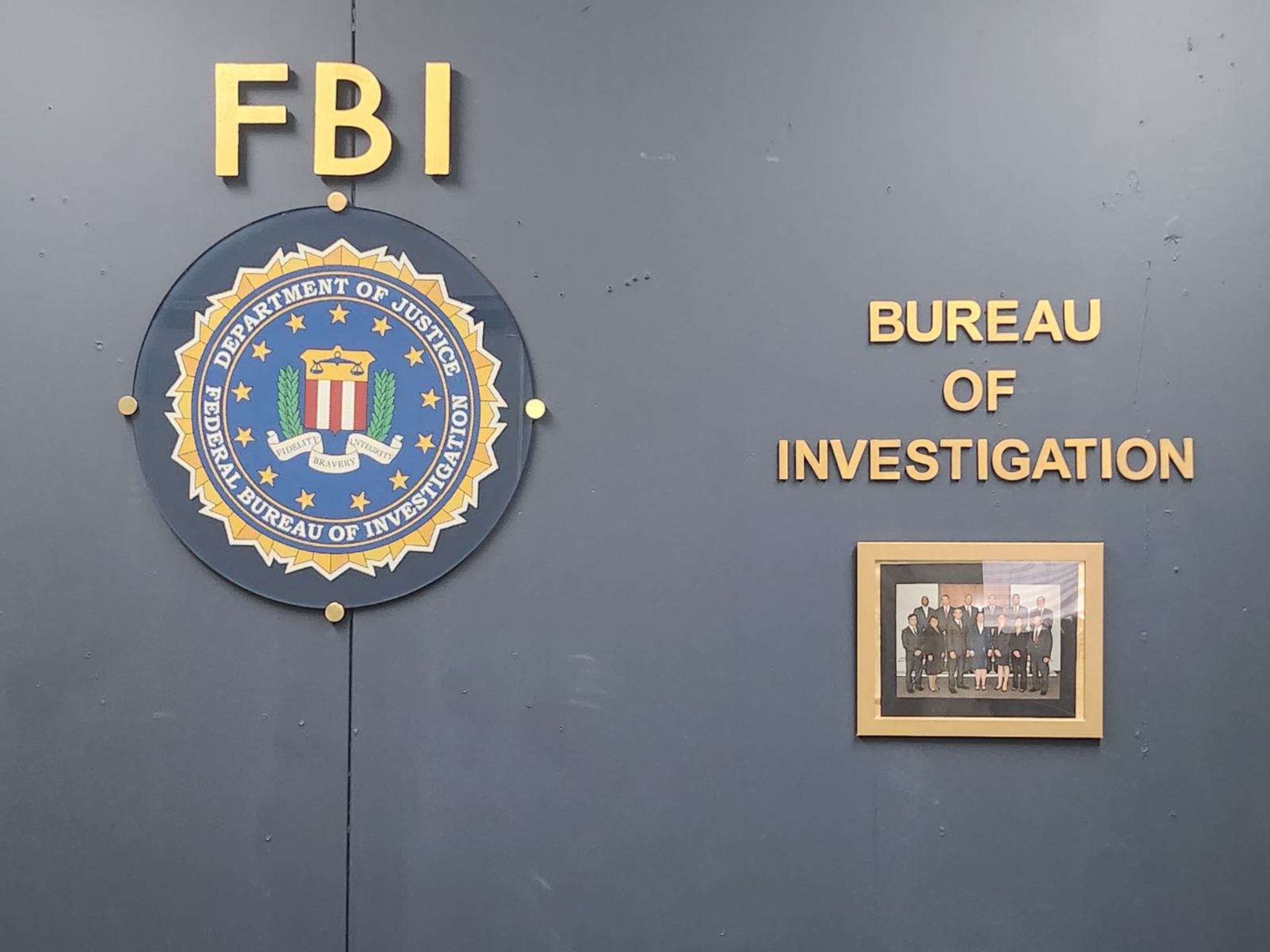 A wall featuring the FBI logo and the words "Bureau of Investigation" alongside a framed group photo.