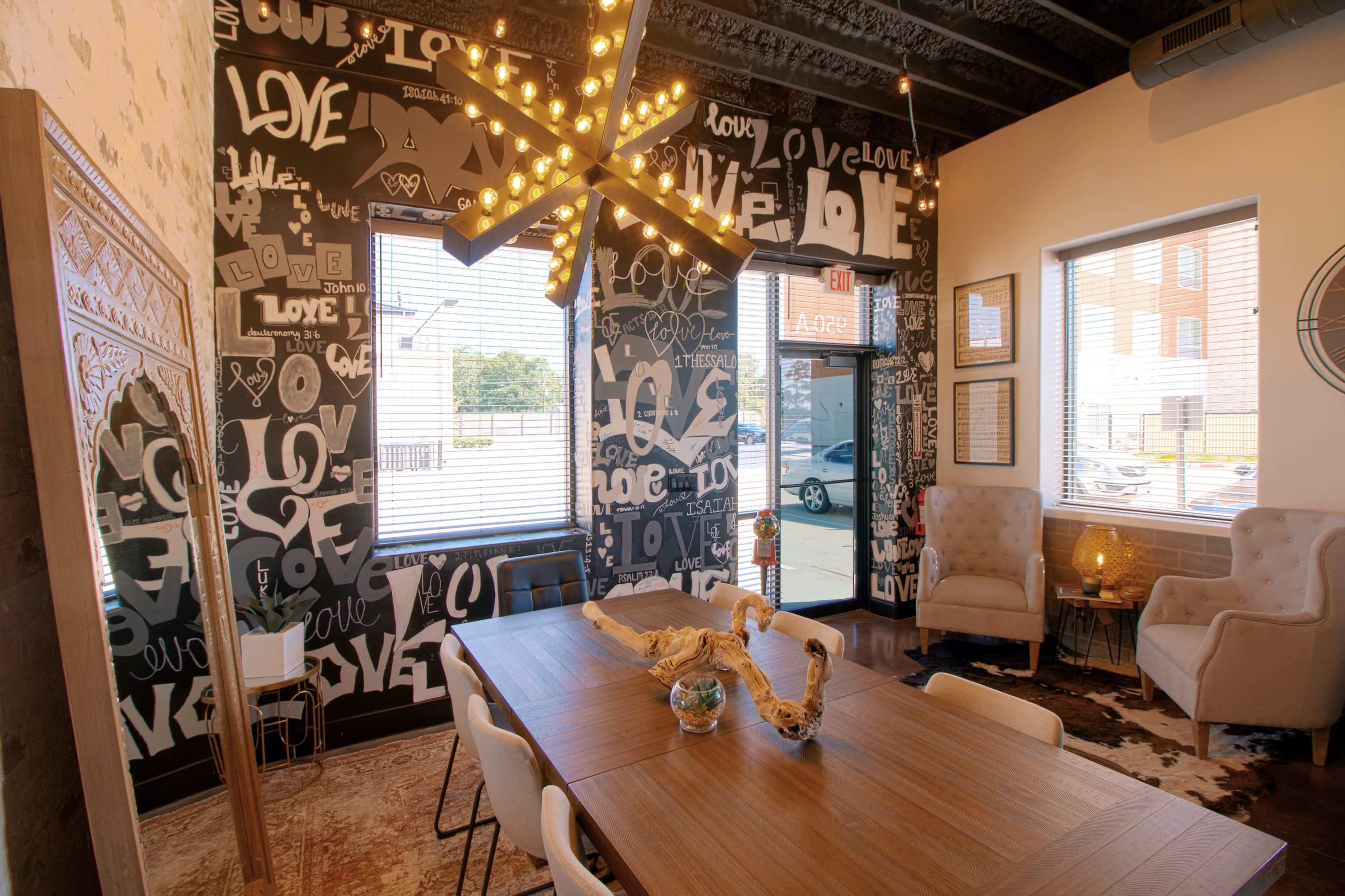 The scene shows a modern dining area with a large wooden table surrounded by white chairs, set against a wall adorned with black and white typographic art that features the word "love."