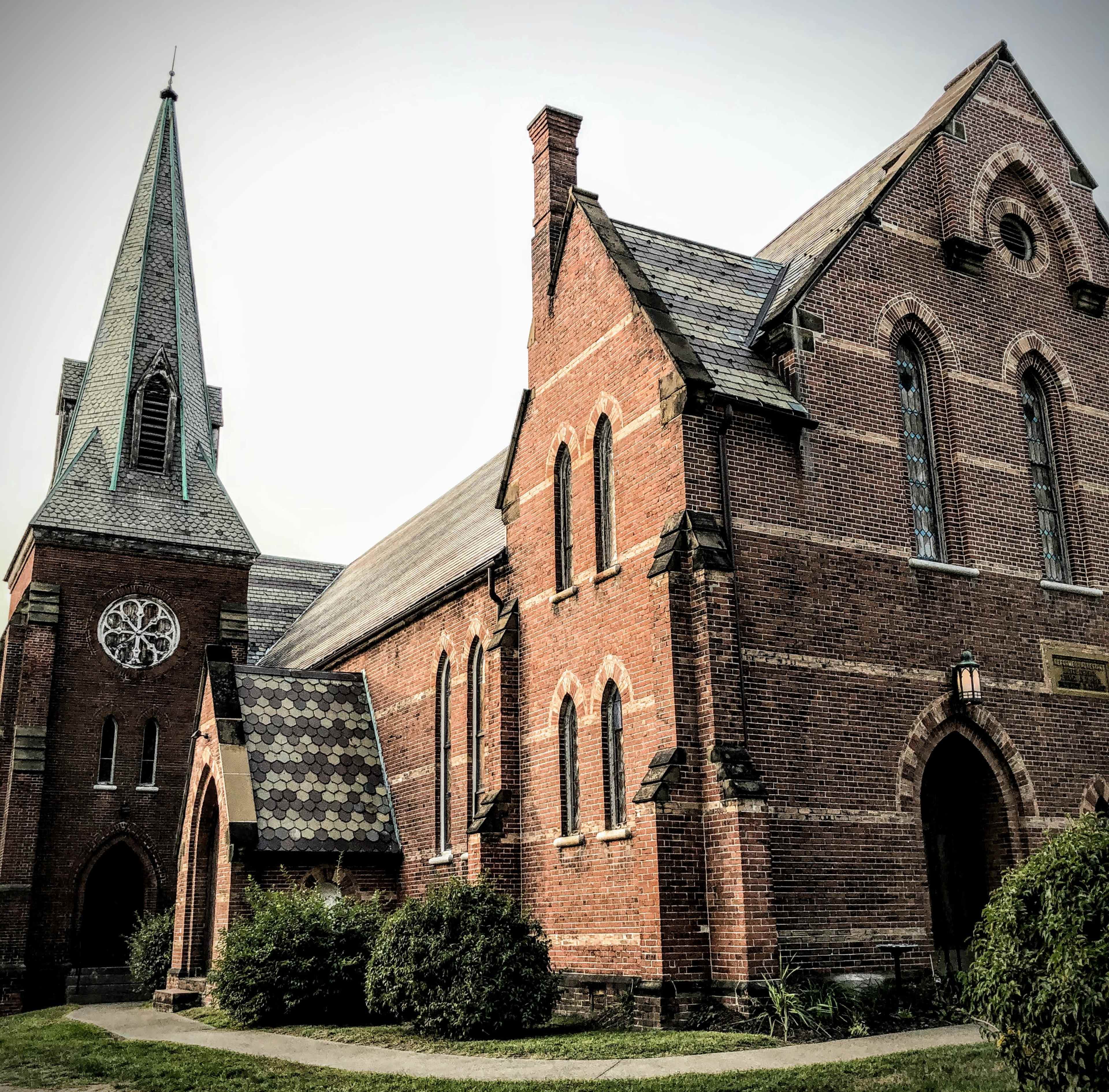 A historic brick church with a tall steeple and stained glass windows.