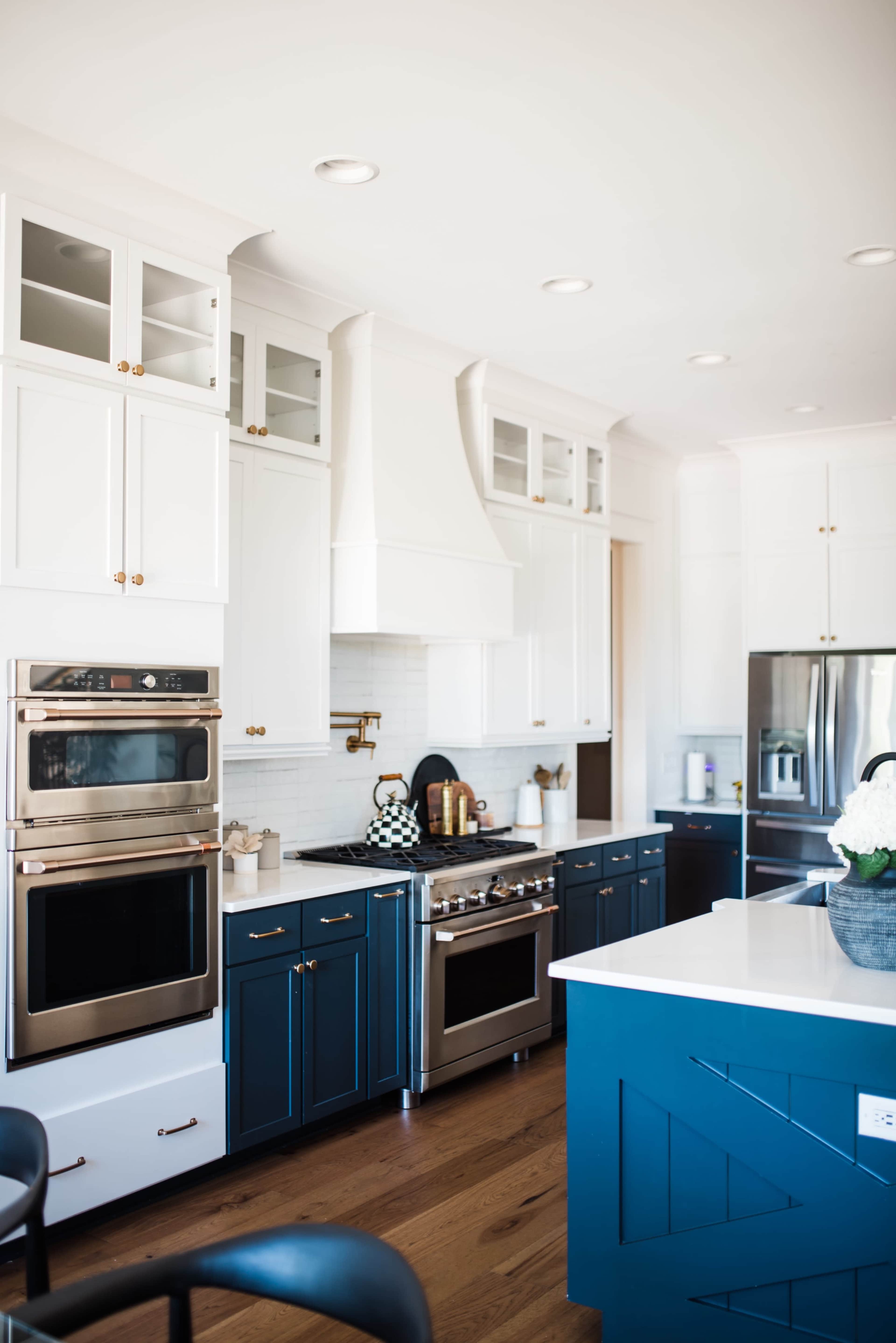 A modern kitchen featuring white upper cabinets, navy blue lower cabinets, stainless steel appliances, and a large island with a countertop.