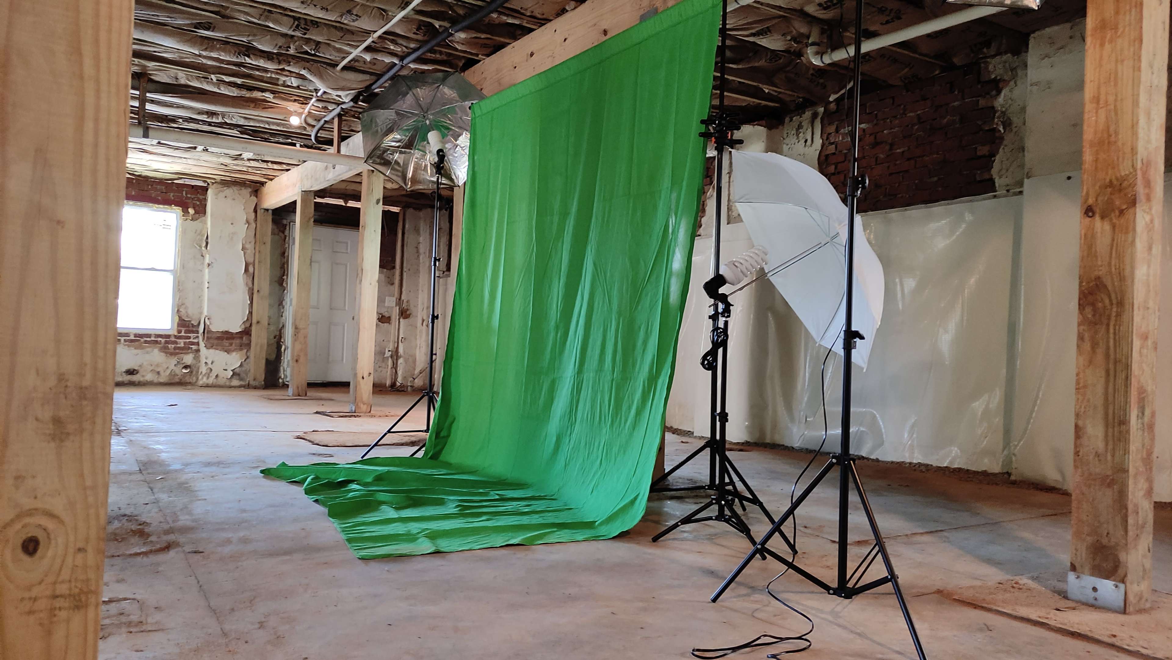 A spacious, unfinished room with a green backdrop setup for photography, accompanied by lighting equipment on stands.