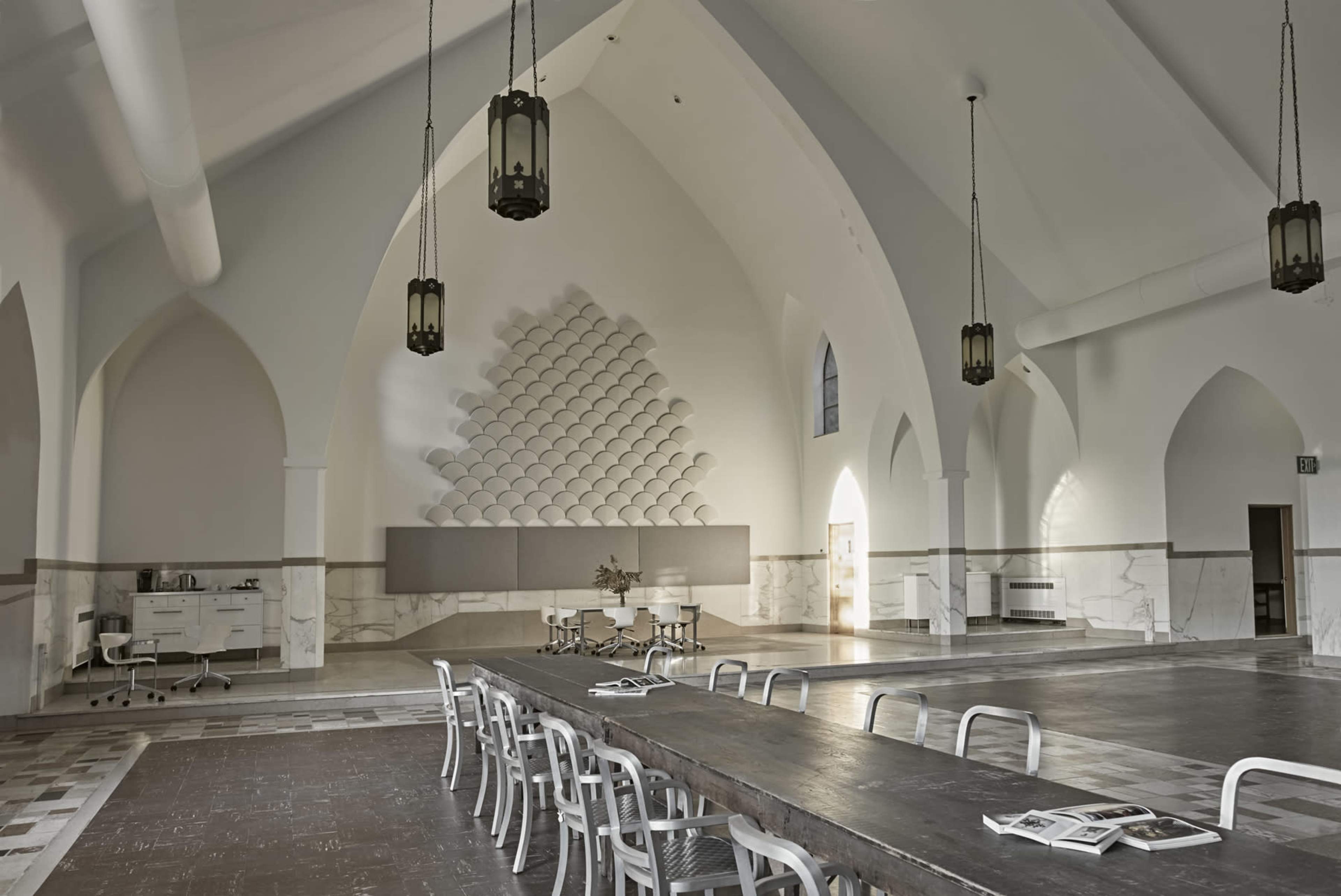 A spacious interior with high arched ceilings, a long wooden table, and minimalist furniture arranged in a bright, airy room.