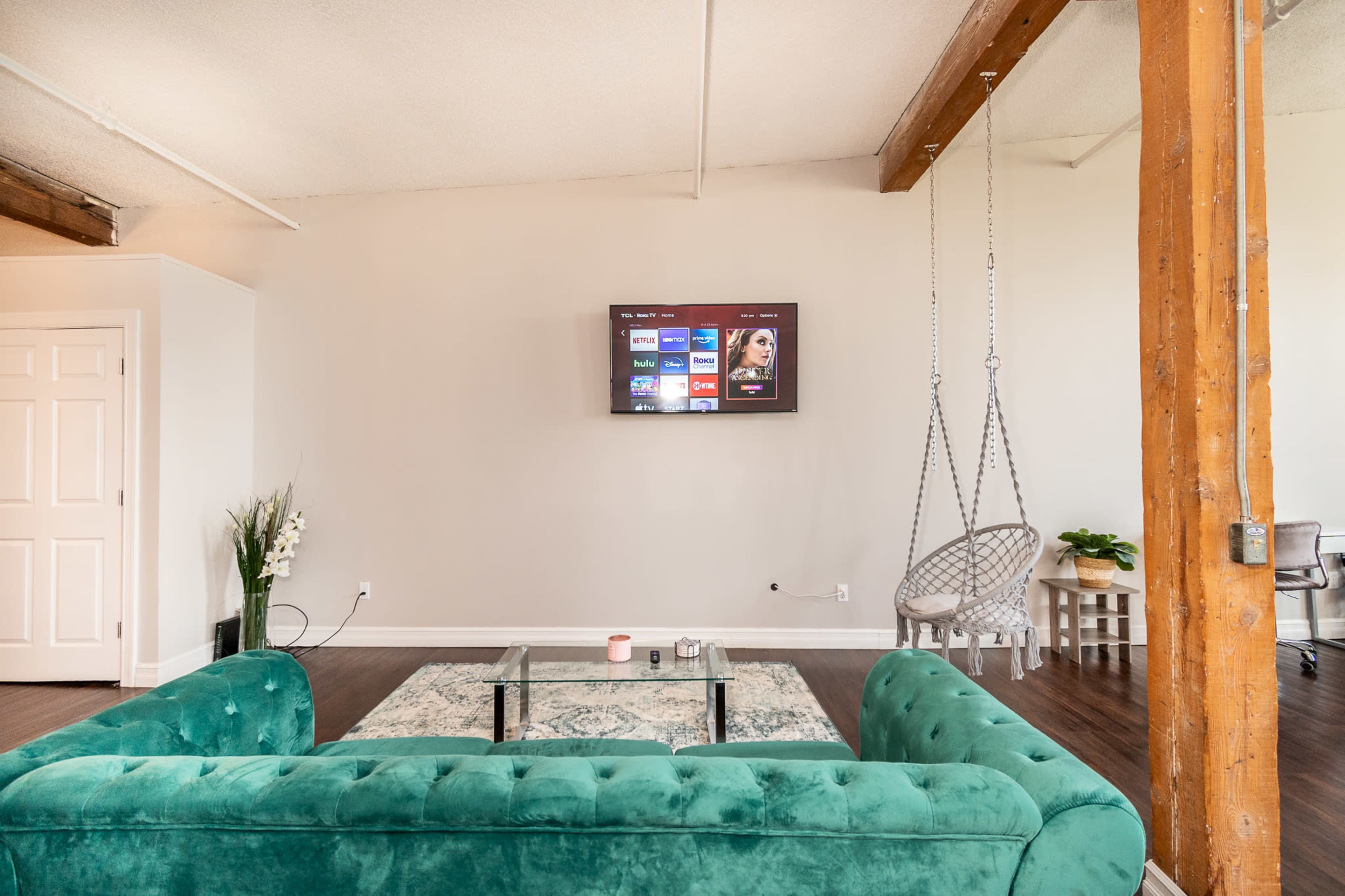 A modern living room with a green velvet sofa facing a wall-mounted television, a hanging chair, and a small table.