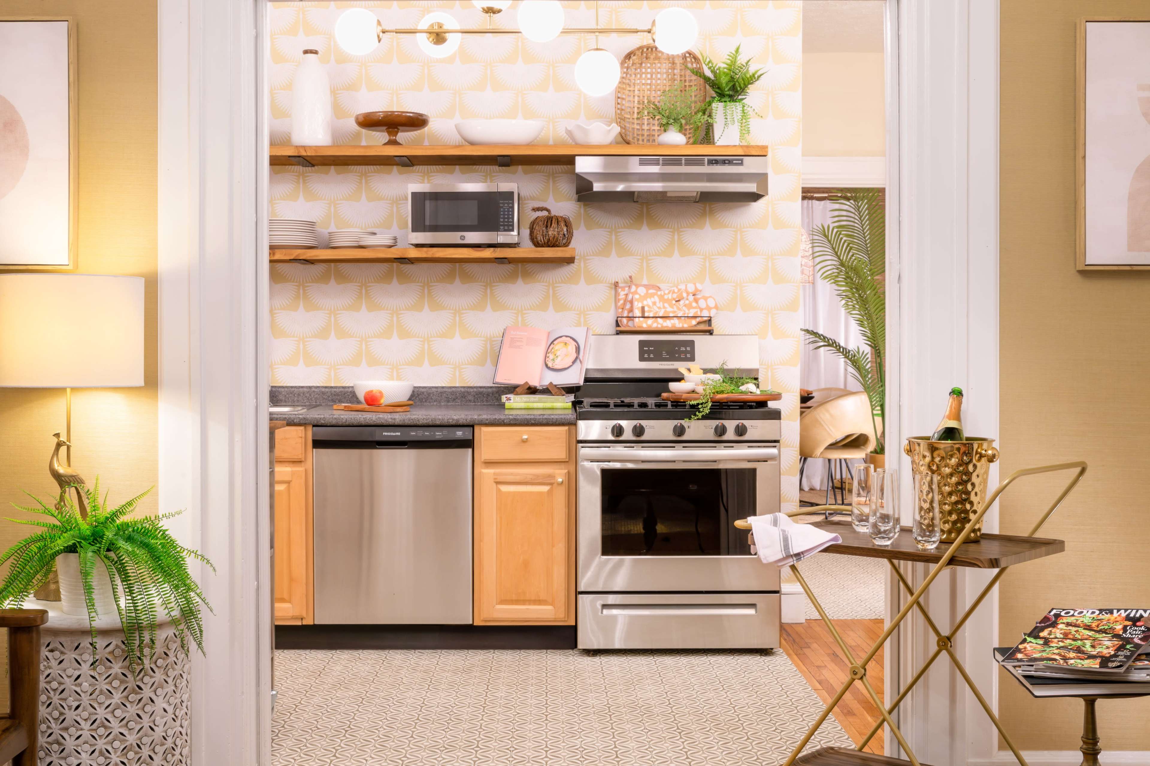 A modern kitchen features stainless steel appliances, wooden cabinetry, and decorative shelving against a patterned wallpaper.