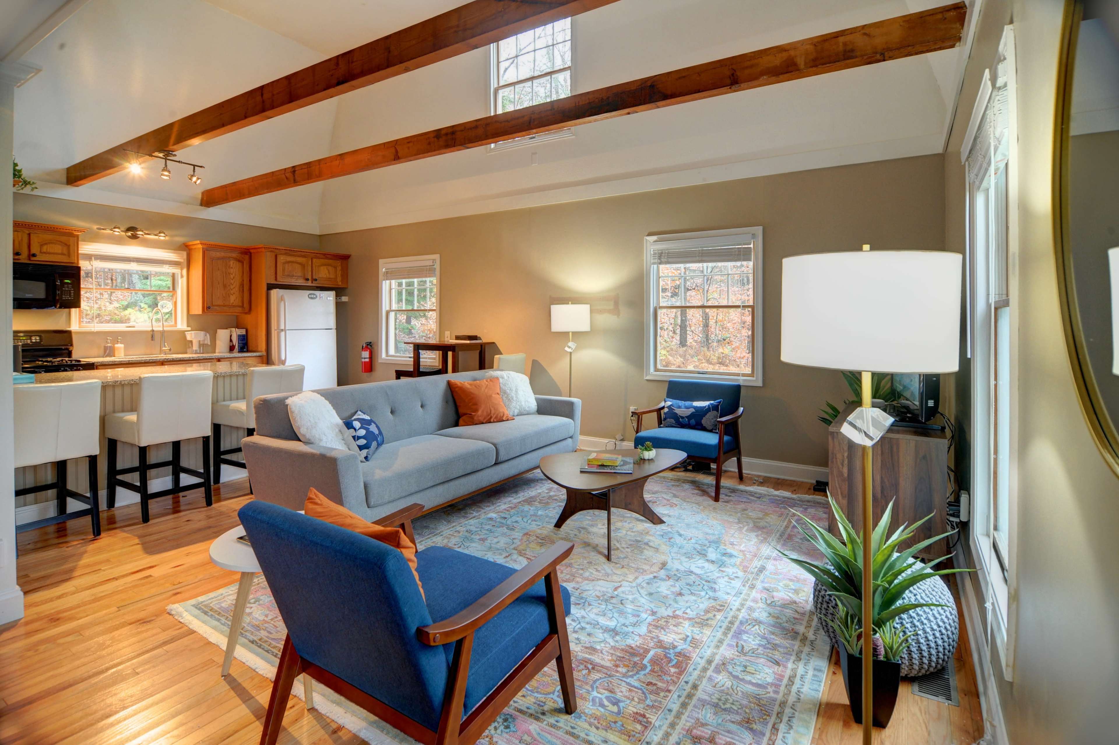 A bright living room with a gray sofa, wooden beams on the ceiling, and a cozy seating arrangement featuring a blue chair and a round coffee table.
