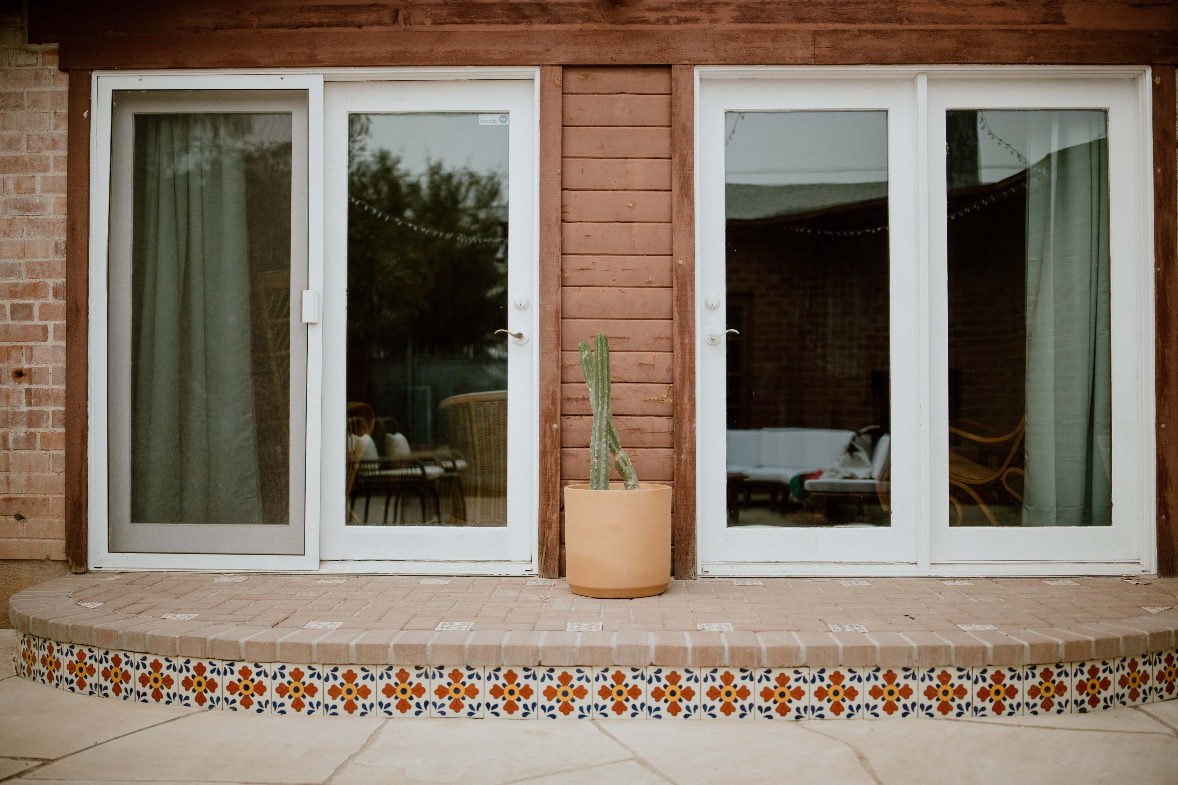 A pair of sliding glass doors leading into a room, surrounded by a tiled step and featuring a potted cactus on the side.