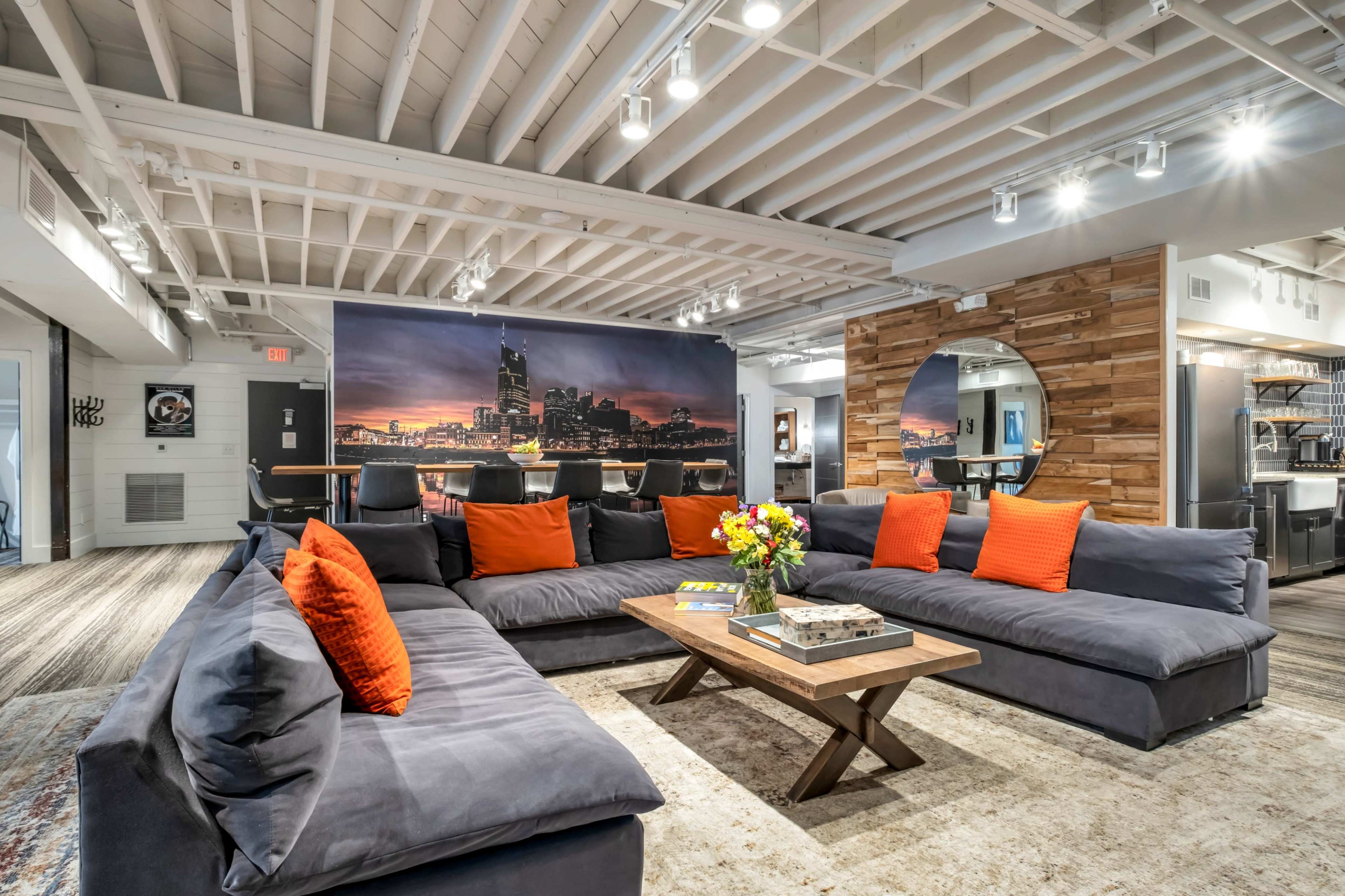 The image shows a modern living room with a large sectional sofa, a wooden coffee table, and a backdrop featuring a city skyline.