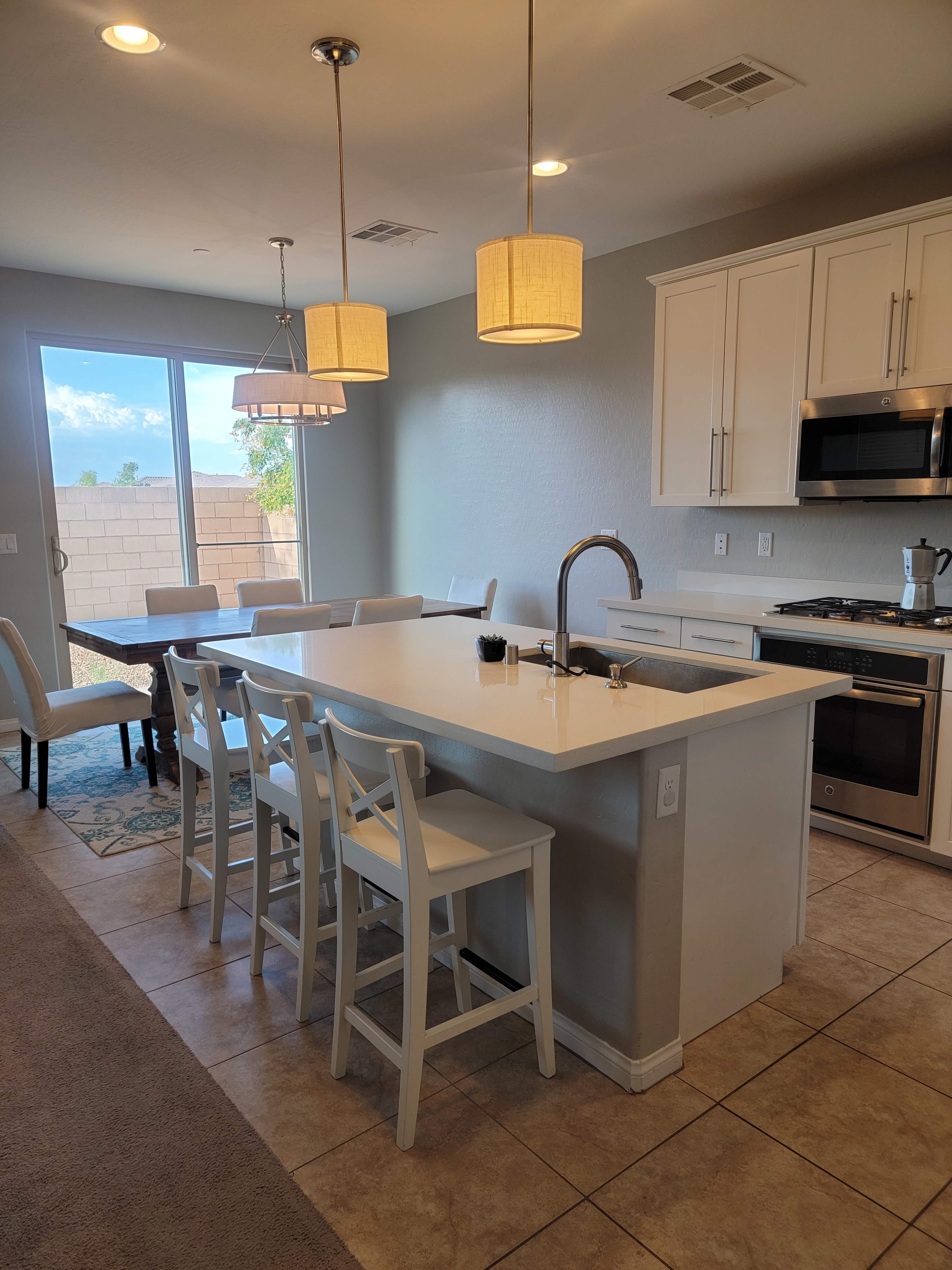 A modern kitchen features a large island with bar stools, a dining table, and sliding glass doors leading to an outdoor area.