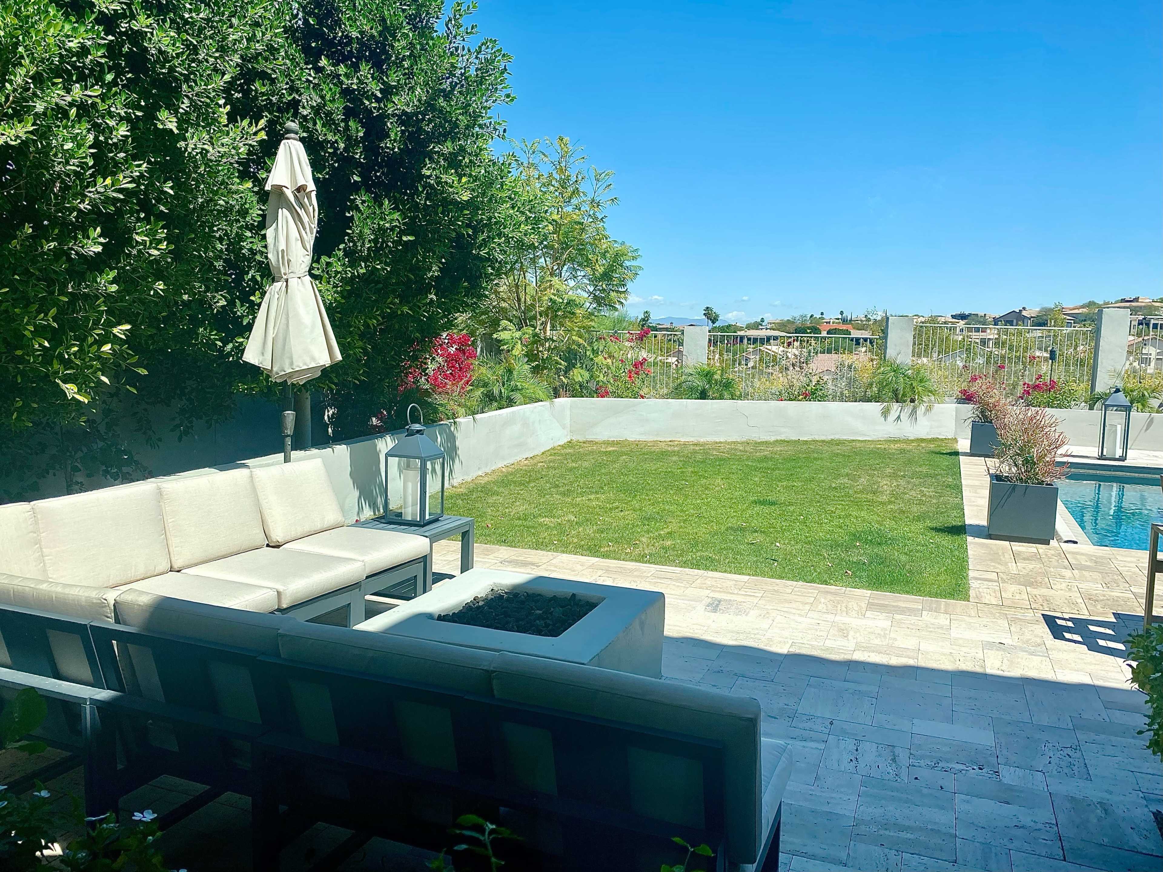 A backyard with a seating area, a lawn, and a swimming pool surrounded by landscaping.