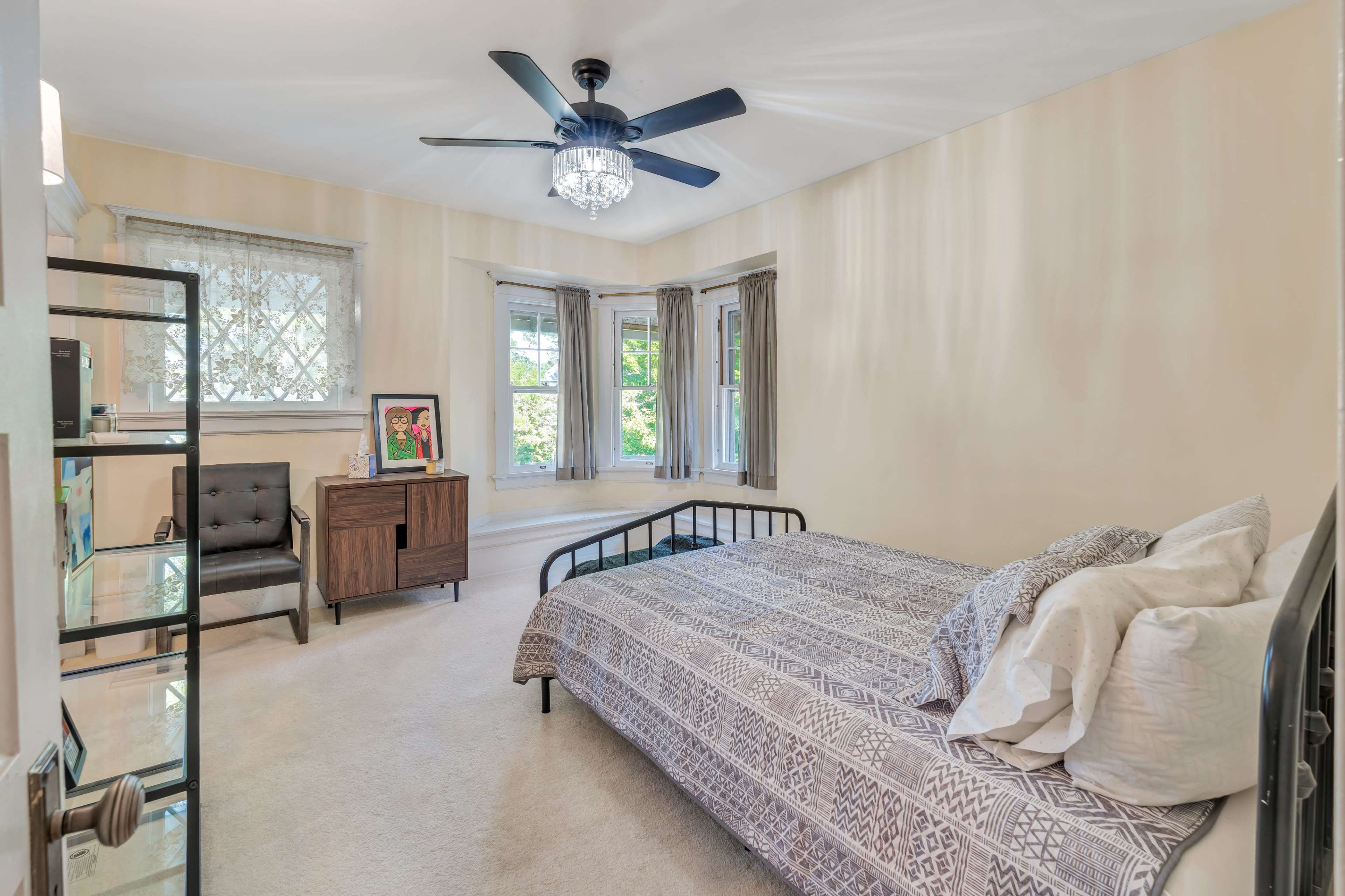 A bedroom with a bed, a wooden nightstand, a chair, and large windows allowing natural light.
