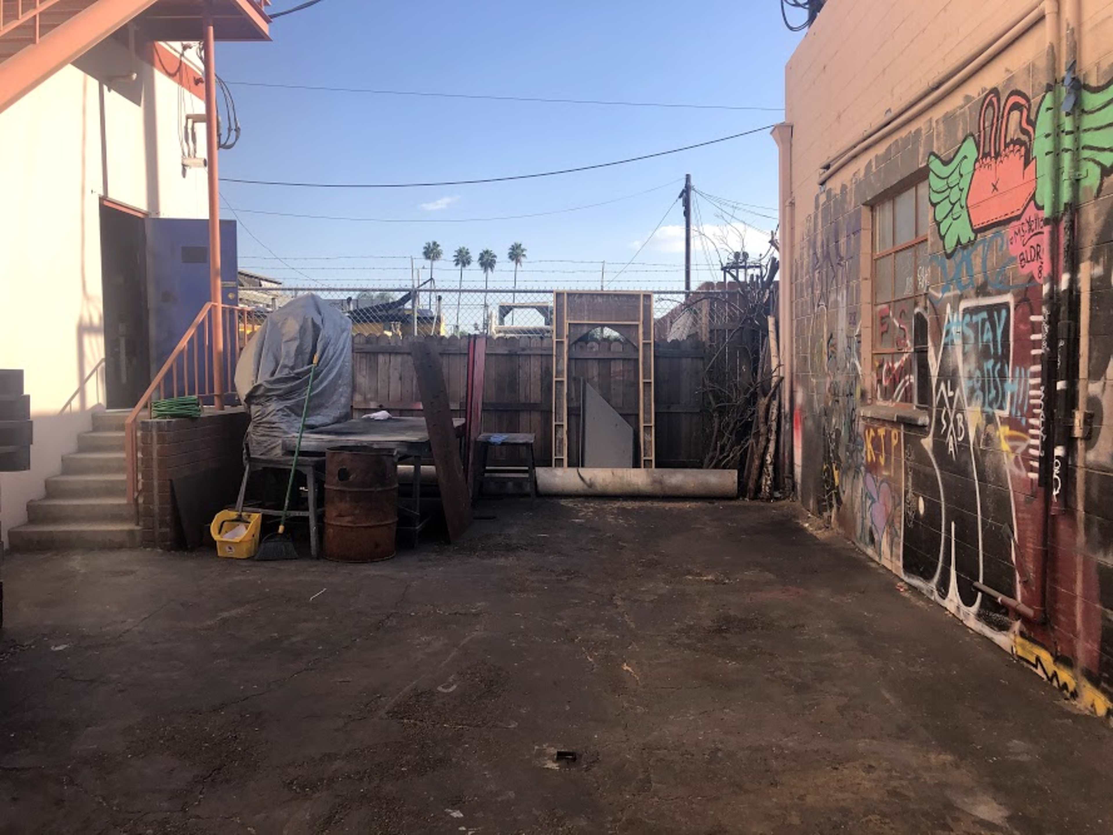 A fenced-in courtyard with scattered debris, a covered table, and graffiti on the wall.