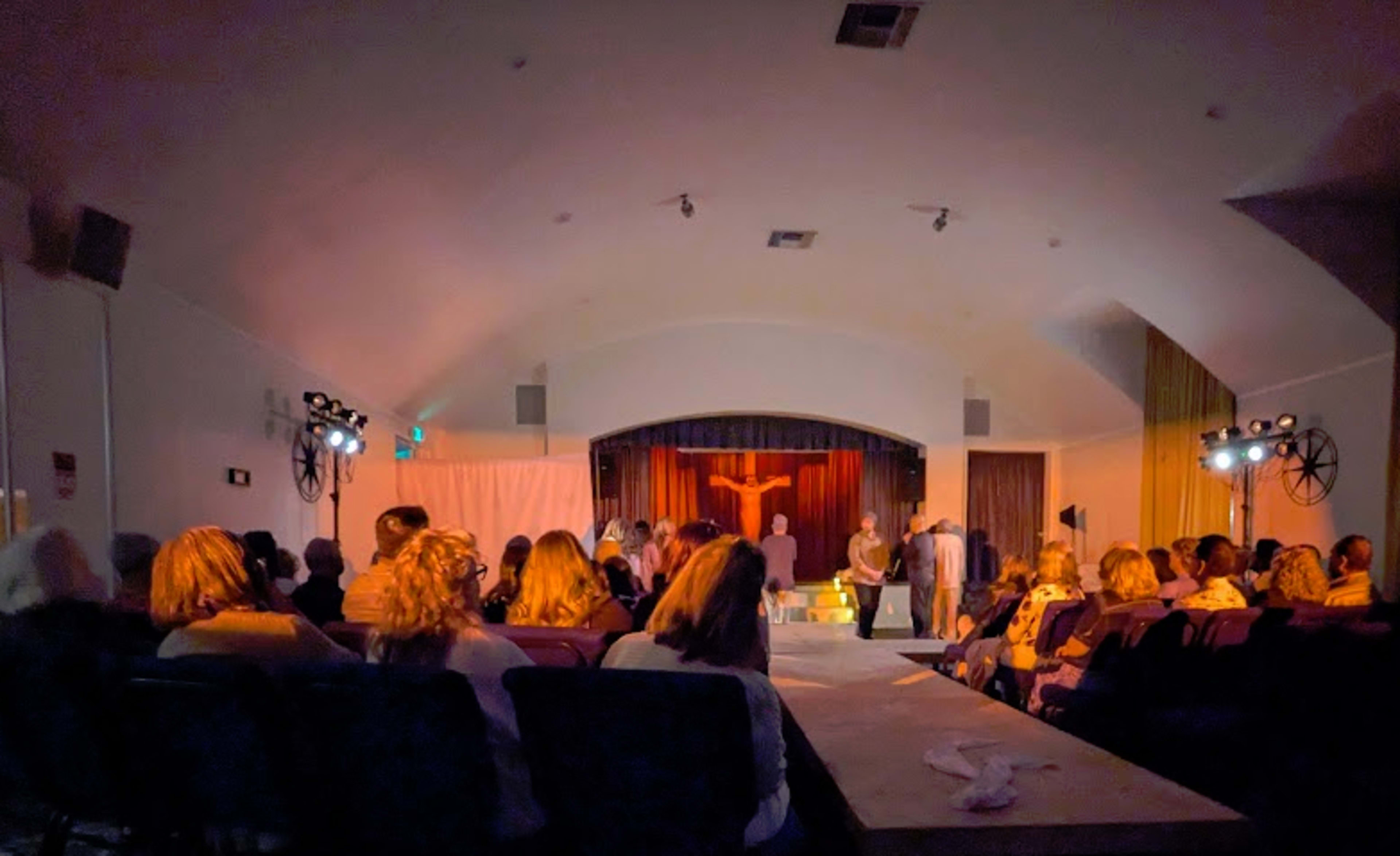 A theater audience watches a performance on stage under dim lighting.