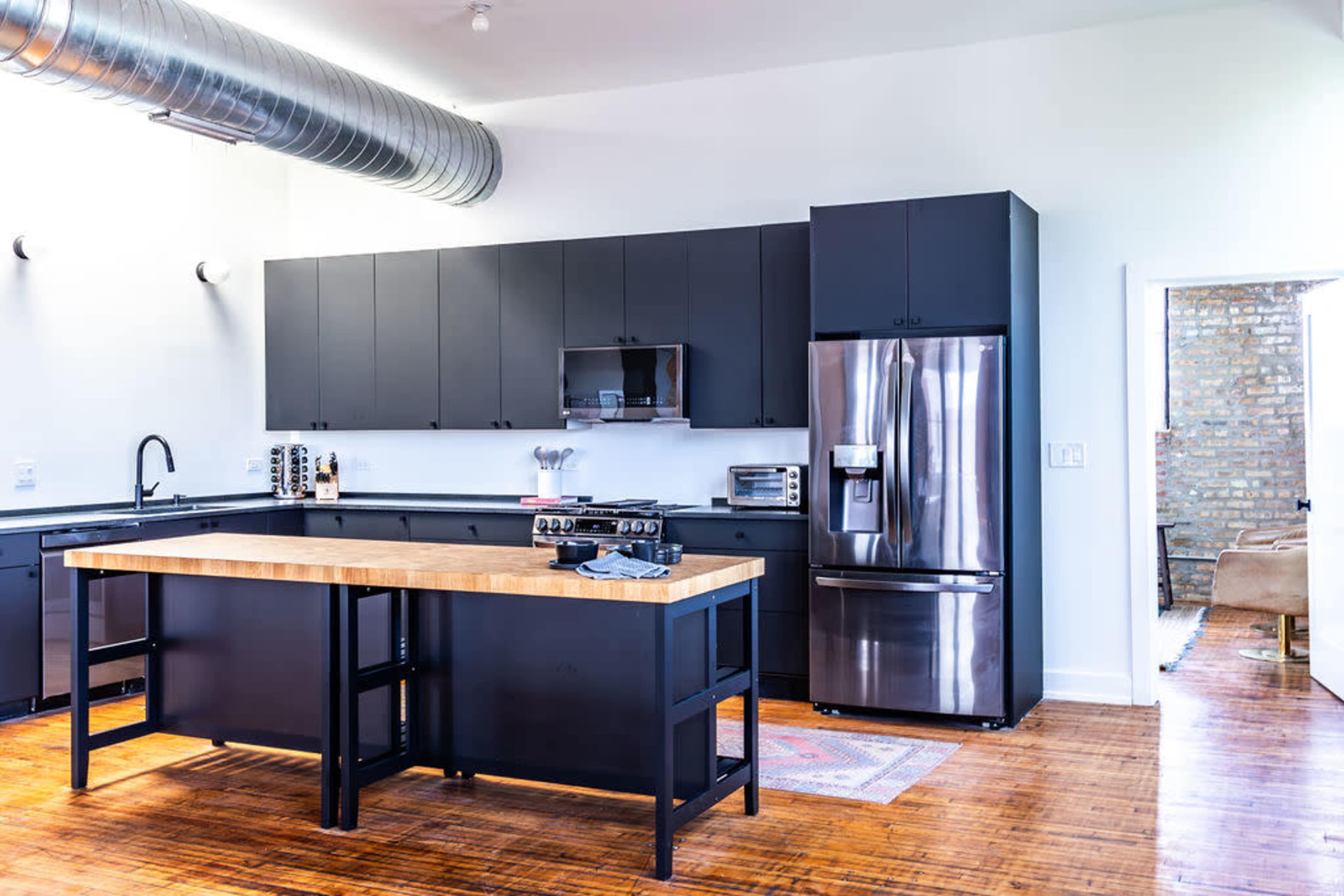 A modern kitchen featuring black cabinetry, a stainless steel refrigerator, and a central wooden island.