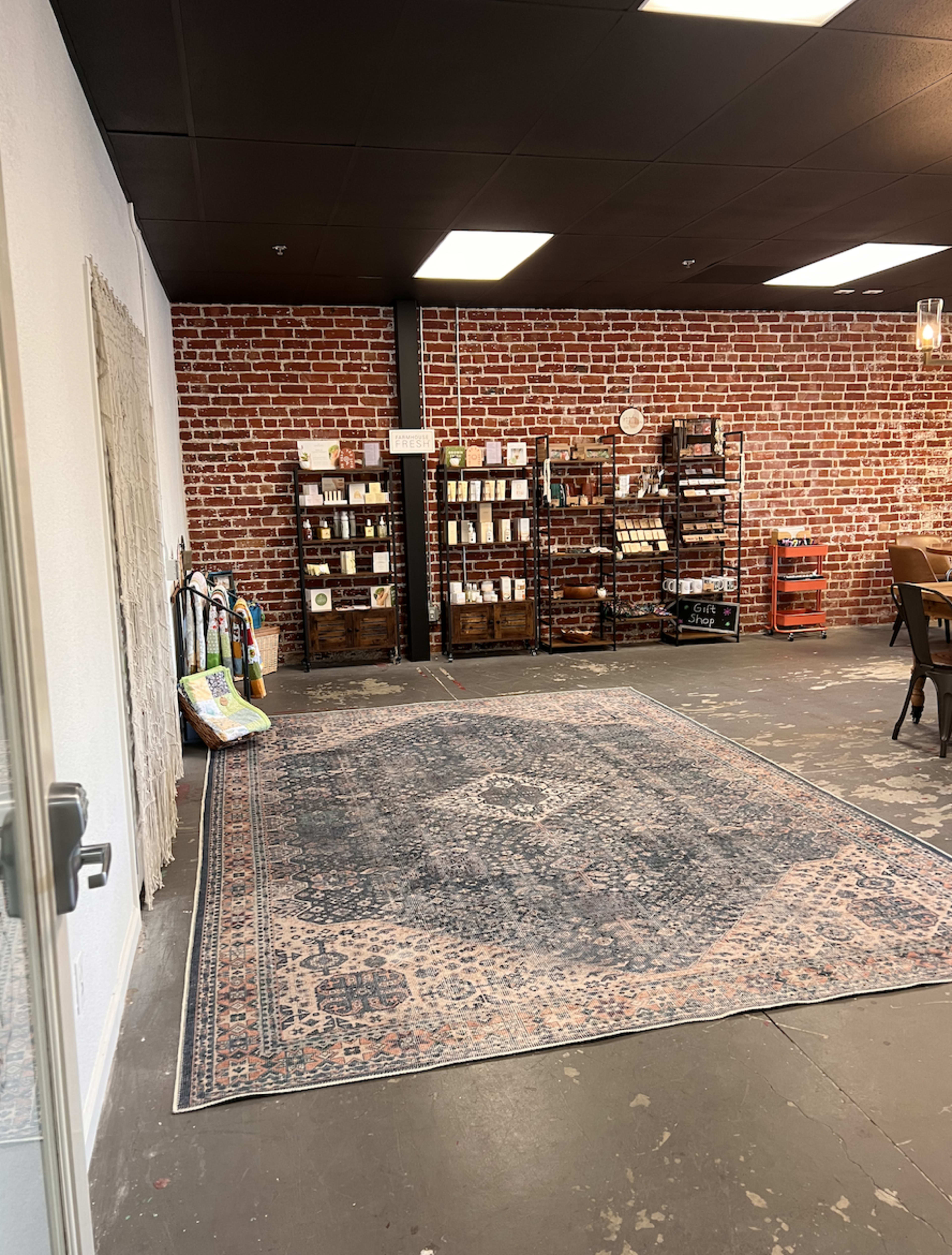 A spacious room with a patterned area rug, exposed brick walls, and wooden shelving units filled with various items.