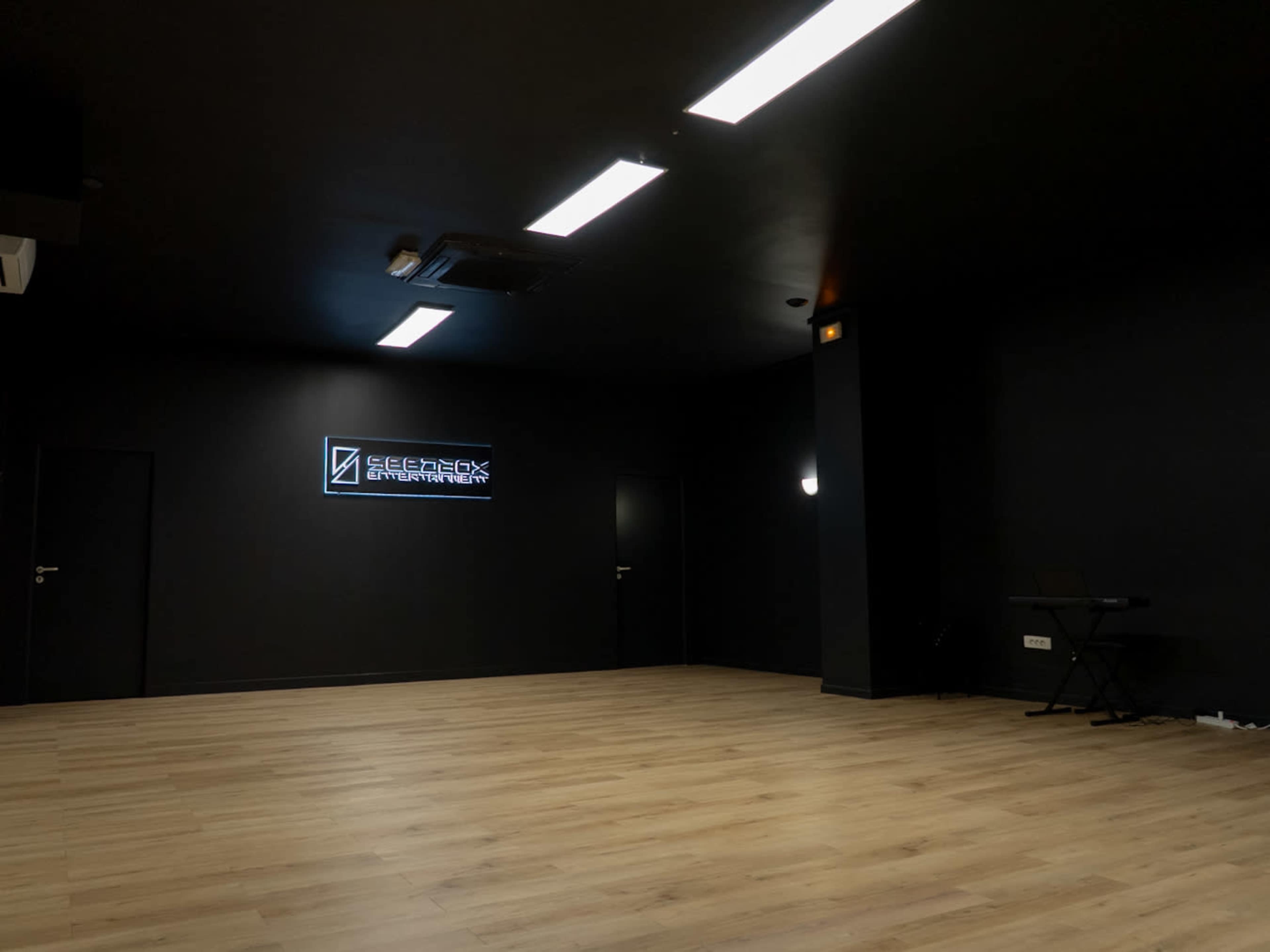 The image shows a dimly lit studio space with black walls, a wooden floor, and a neon sign that reads "GENLOCK ENTERTAINMENT" mounted on the wall.